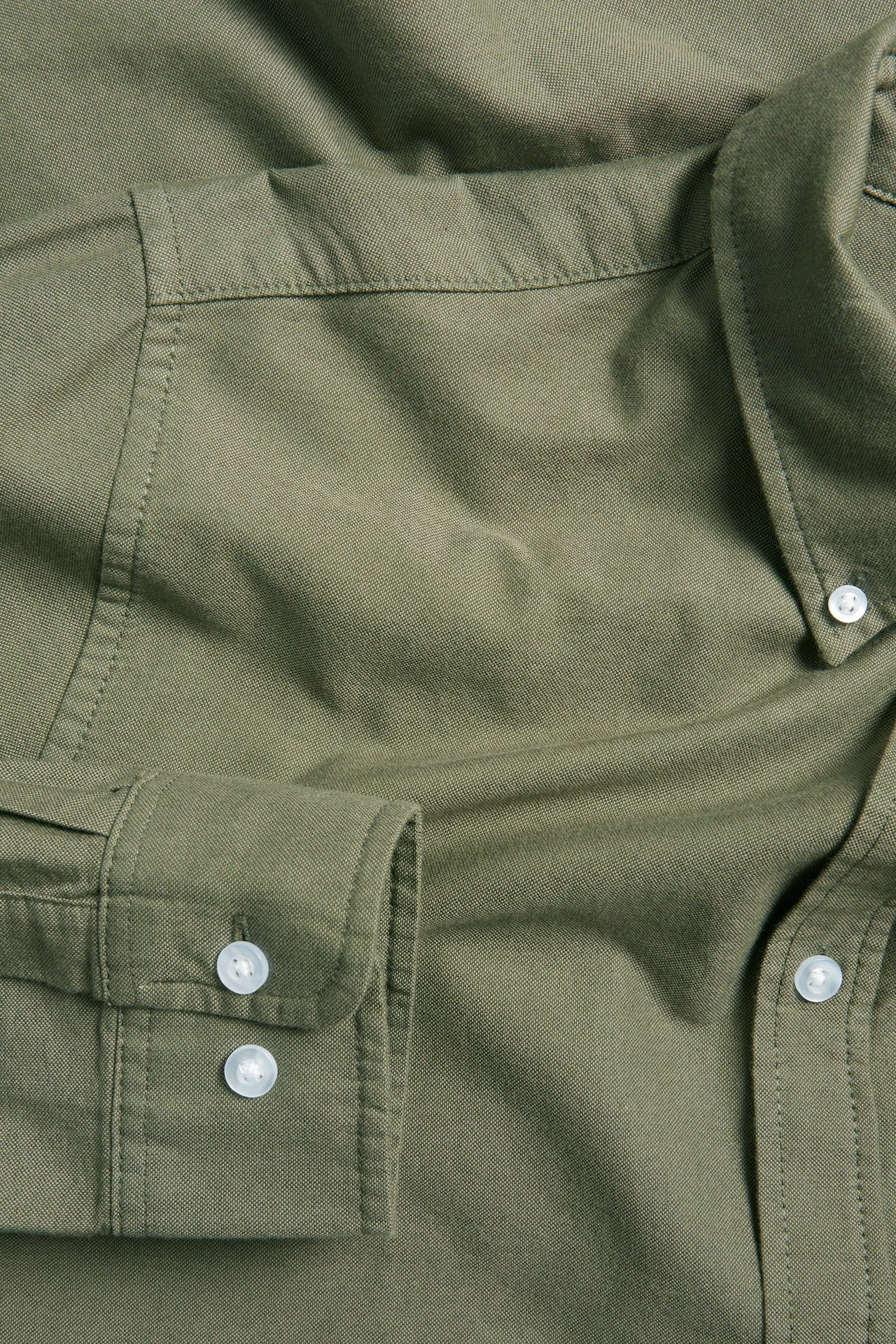 Närbild på en herr olivgrön melerad bomulls oxfordskjorta med button-down krage och vita knappar.