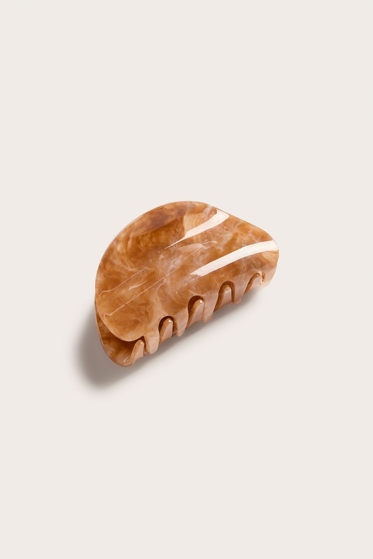 Lähikuva beigestä kuvioidusta hiusklipsistä, joka on valmistettu kiiltävästä materiaalista.