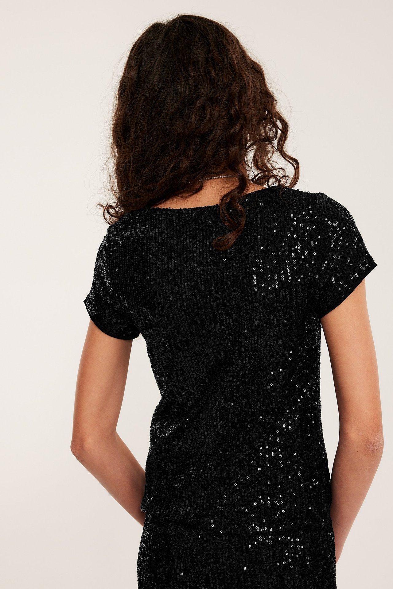 Bakifrån på ett barn som bär en svart kortärmad paljettopp och matchande svart paljettkjol.