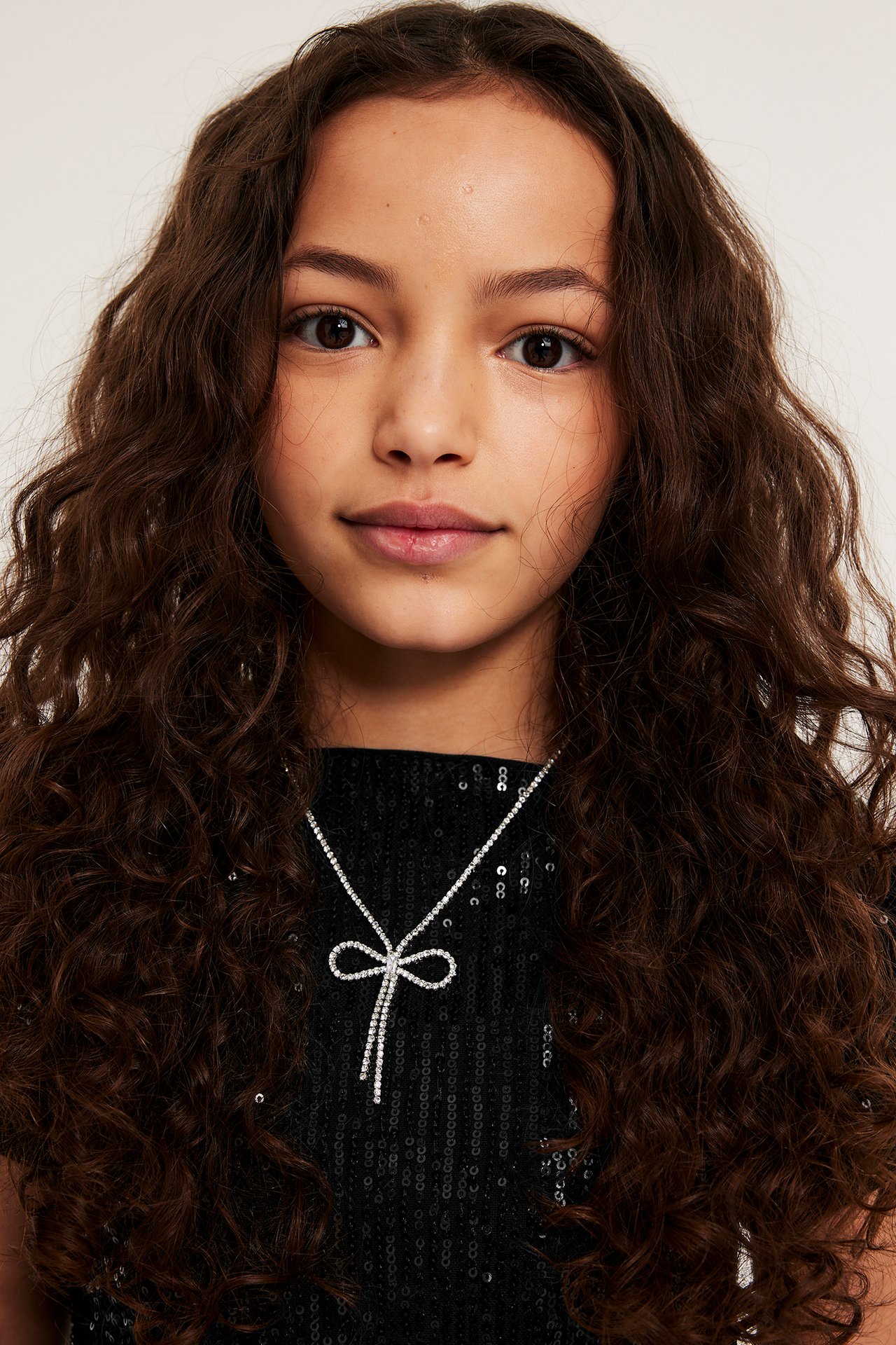 Närbild, framifrån, på ett barn i svart kortärmad paljettopp och ett halsband med strassrosett.