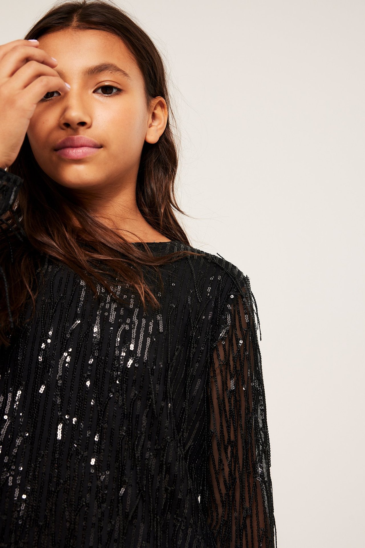 Närbild, framifrån, på ett barn i svart långärmad topp med glittrande paljettfransar.