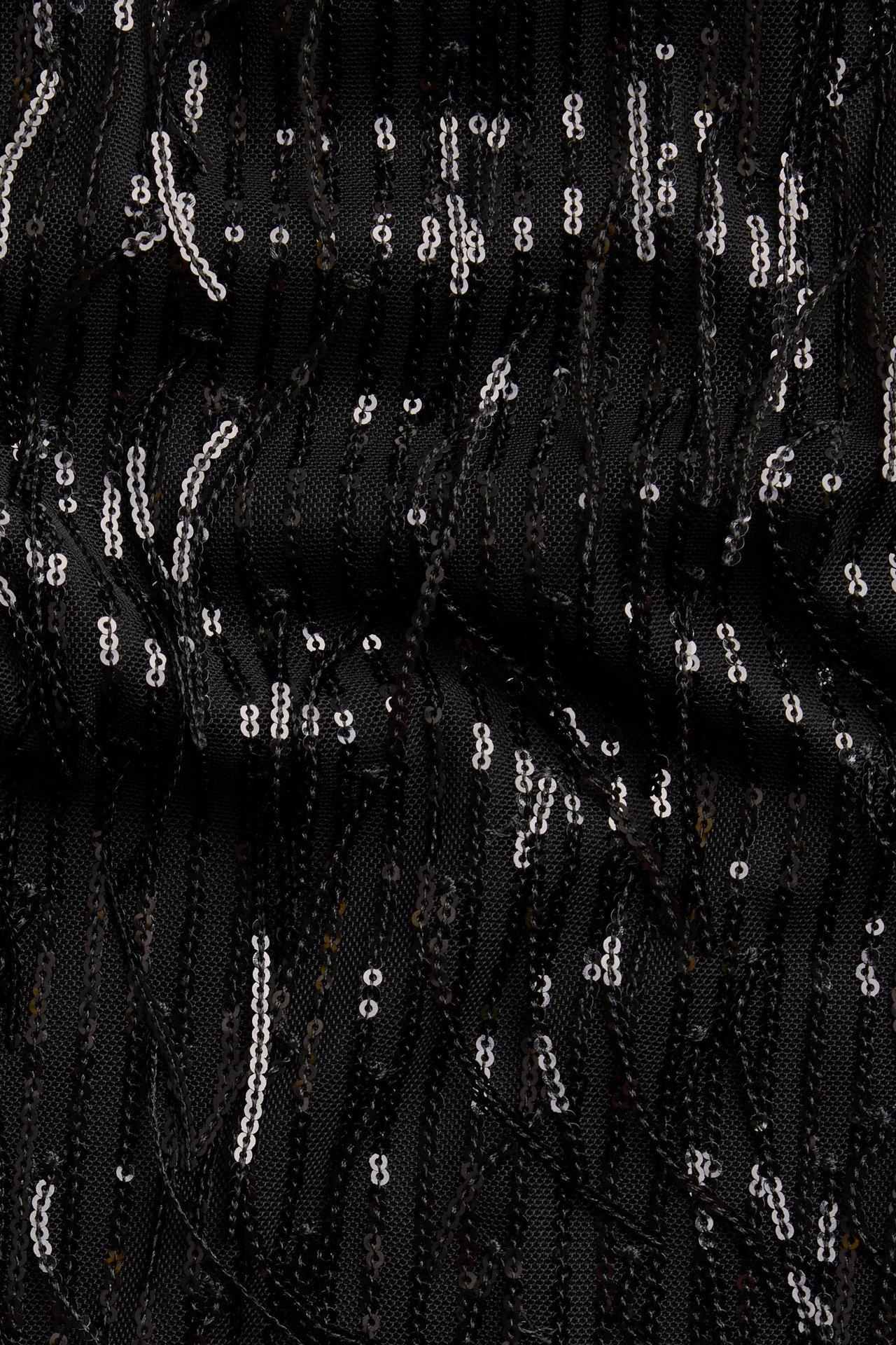 Zbliżenie czarnego materiału na top, z wiszącymi czarnymi i srebrnymi frędzlami z cekinów.