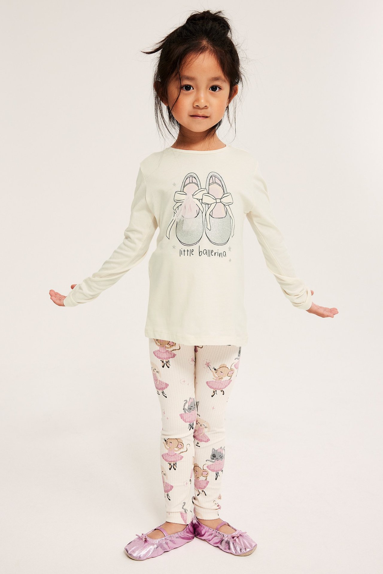 Widok z przodu: Dziecko w bluzce ecru z nadrukiem baletek, wzorzystych legginsach i różowych baletkach.