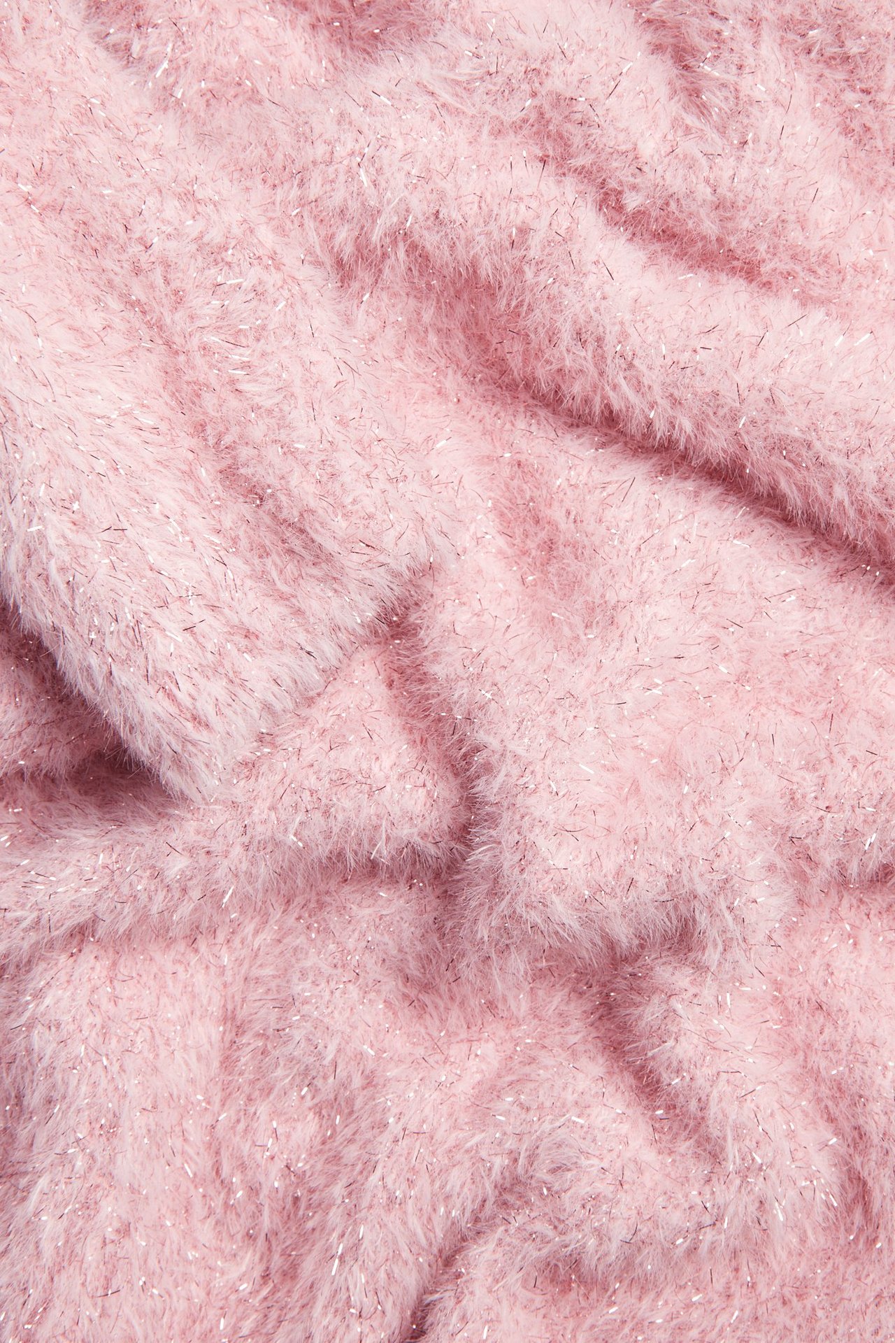 Zbliżenie na miękki, puszysty jasnoróżowy materiał dzianinowy z mieniącymi się srebrnymi brokatowymi nićmi.