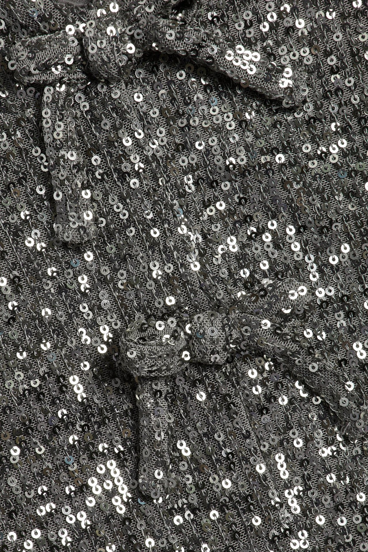 Zbliżenie szarego topu z cekinami i ozdobnymi kokardkami na błyszczącym materiale.