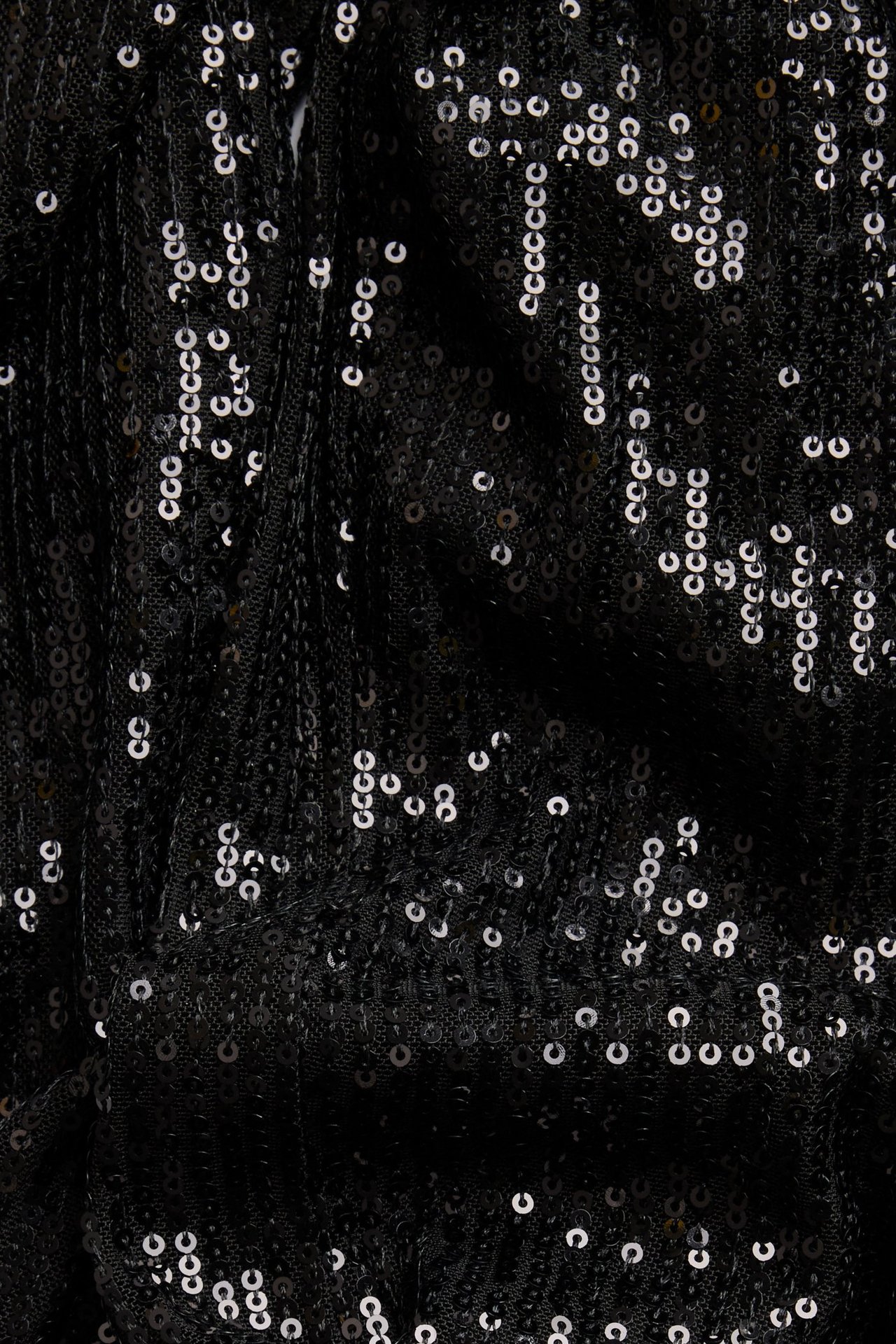 Lähikuva mustasta paljettihousujen kankaasta, joka näyttää kiiltävän, kuvioidun glitterkuvion.