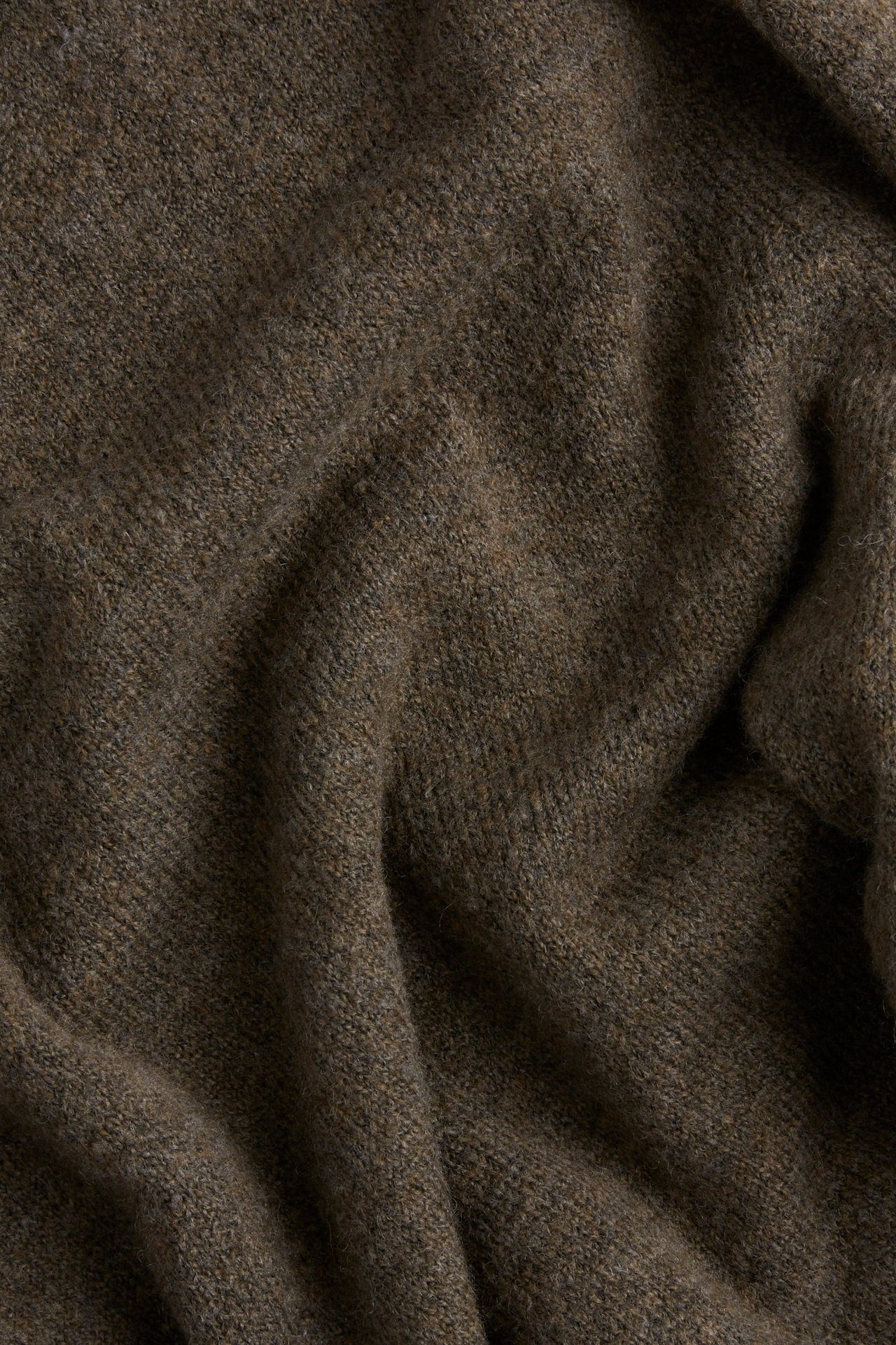 Zbliżenie na brązowy, dzianinowy materiał swetra z widoczną teksturą i miękkimi fałdami.