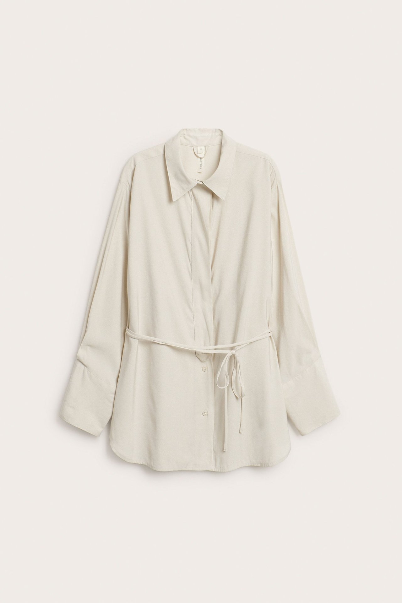 Forfra, lys beige oversized viskoseblanding skjorte med skjult knepping og knyttet stoffbelte.