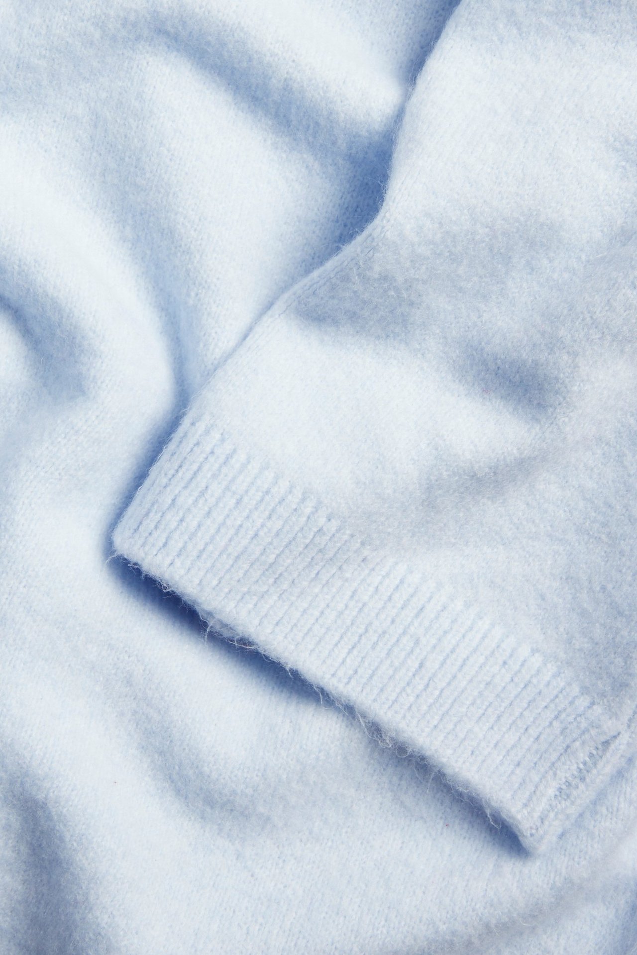 Zbliżenie jasnoniebieskiego, miękkiego swetra dzianinowego z widocznym ściągaczem.