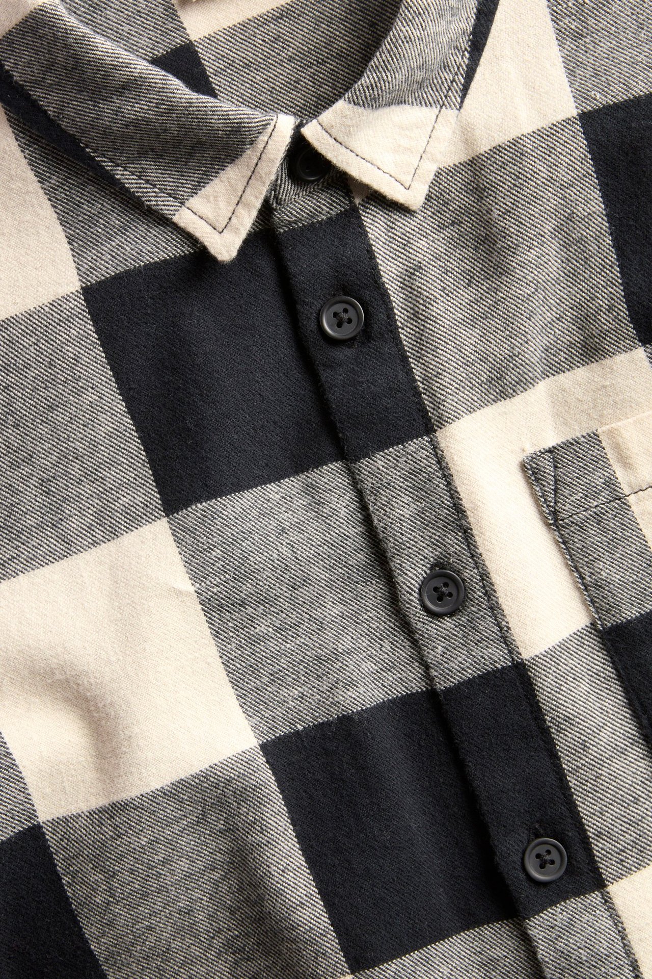Zbliżenie na czarno-beżową koszulę flanelową w kratę z czarnymi guzikami i kieszenią na piersi.