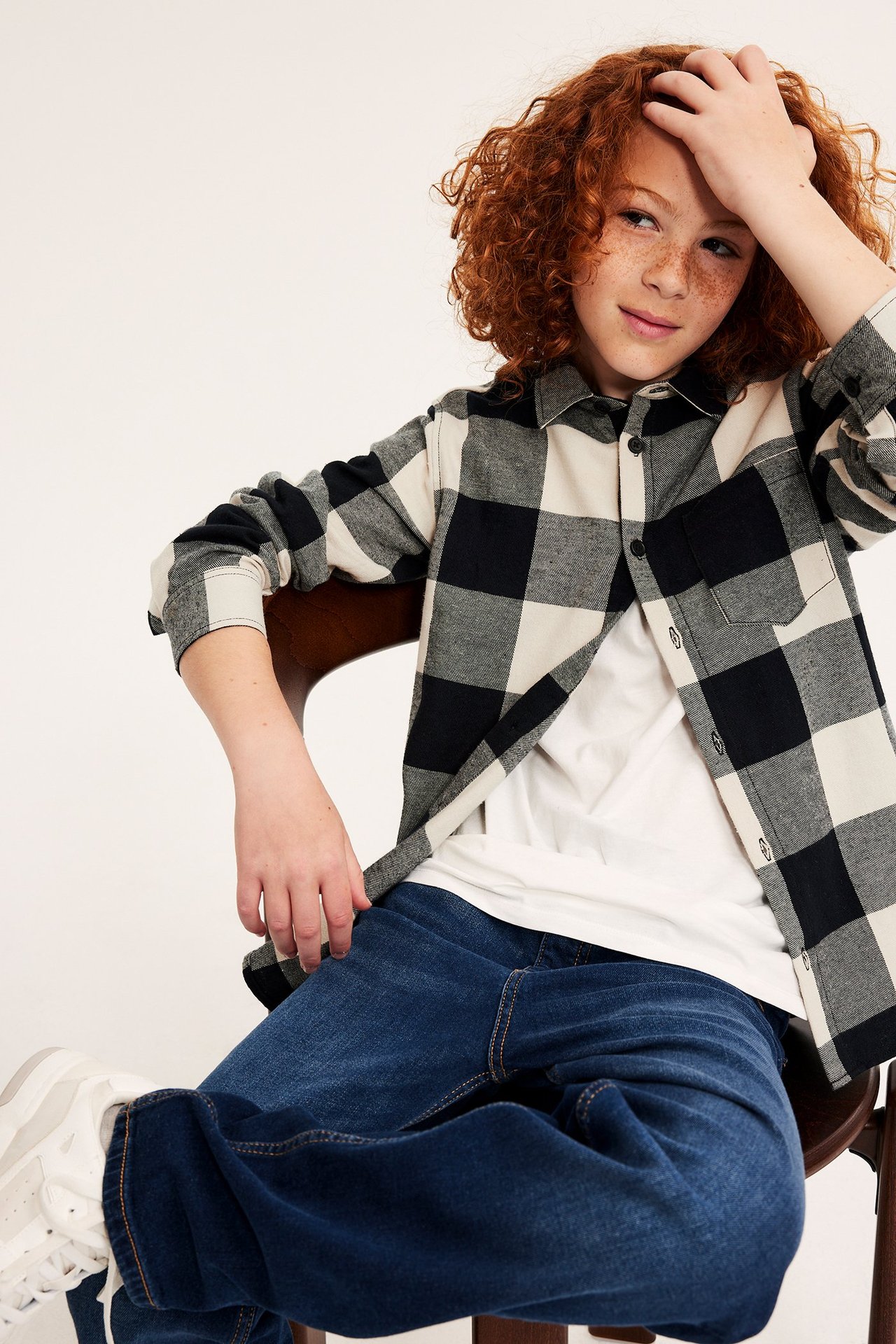 Framifrån: Barn bär öppen svart- och vitrutig flanellskjorta över vit t-shirt och blå jeans.