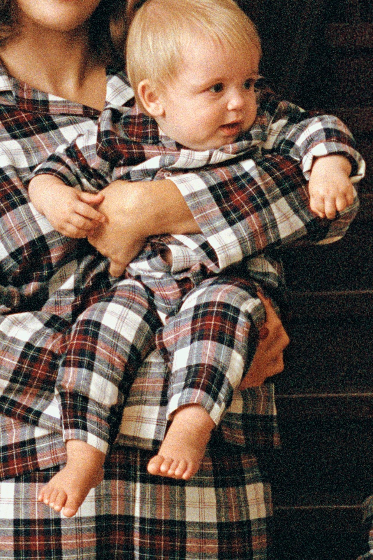 Edestä, vauva yllään ruudulliset luonnonvalkoiset, punaiset ja mustat flanellipyjamat, aikuinen pitää kiinni vastaavissa yöasuissa.