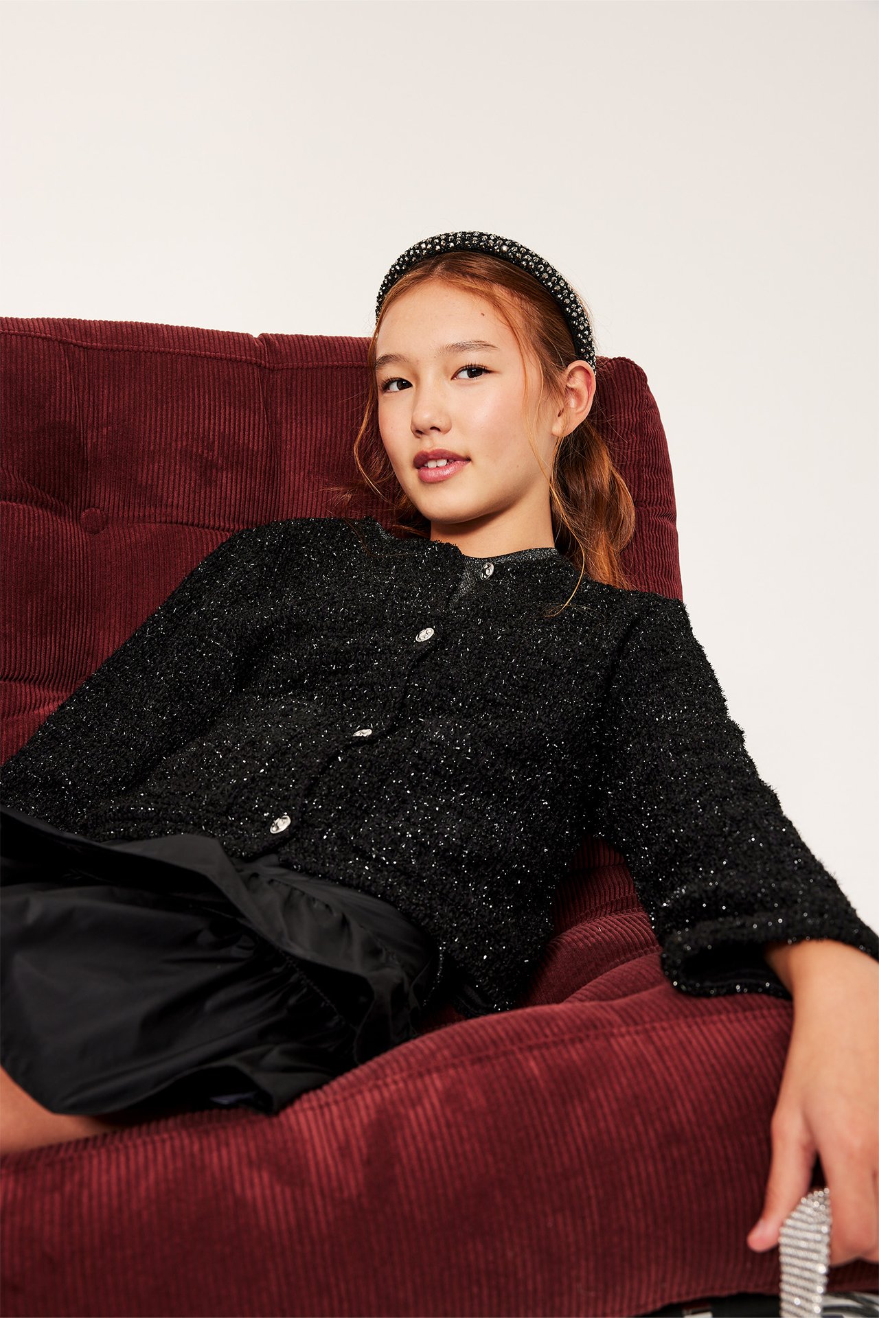 Czarna jacquardowa kurtka na młodej kobiecie, siedzi na czerwonej sztruksowej kanapie.