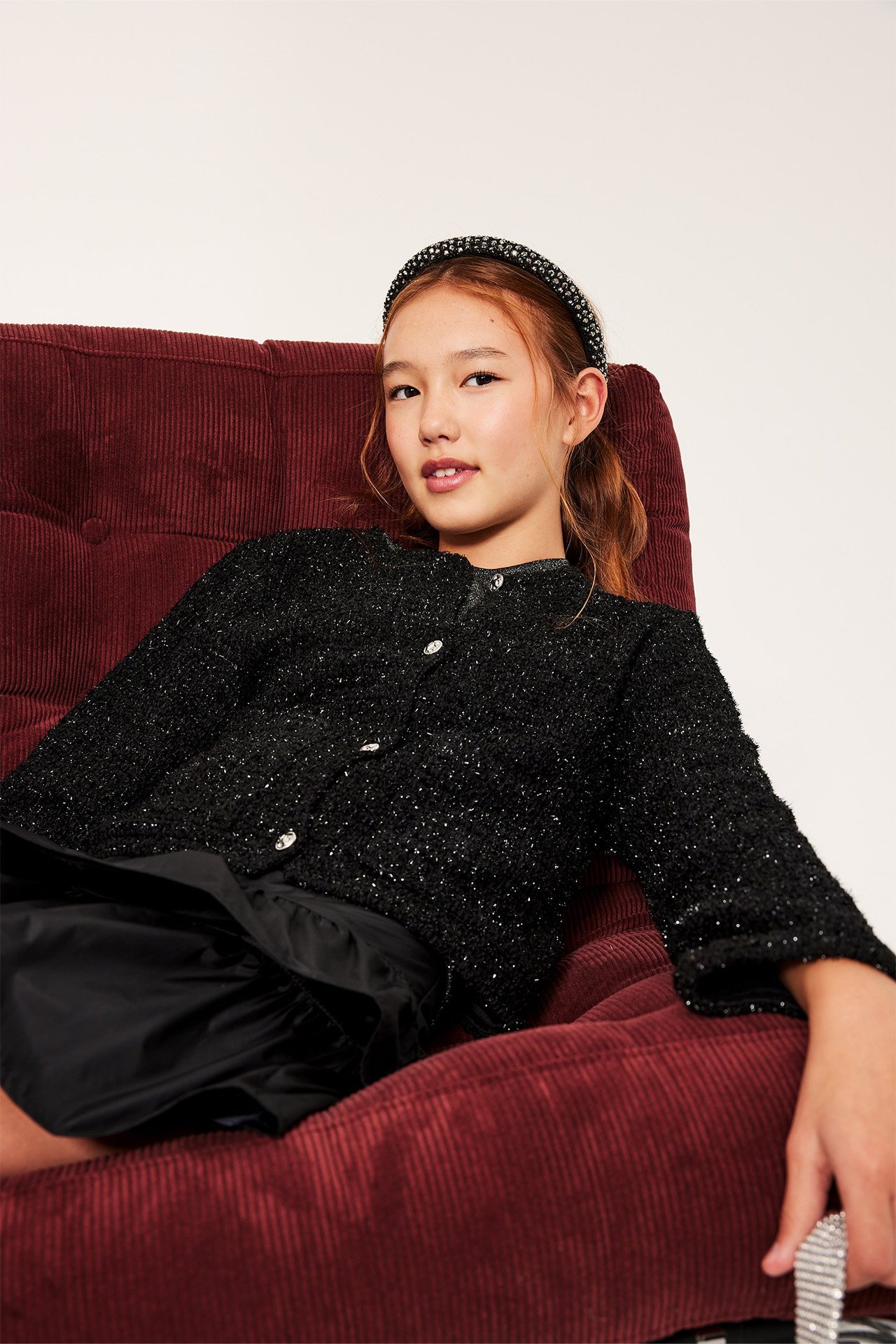 Czarna jacquardowa kurtka na młodej kobiecie, siedzi na czerwonej sztruksowej kanapie.