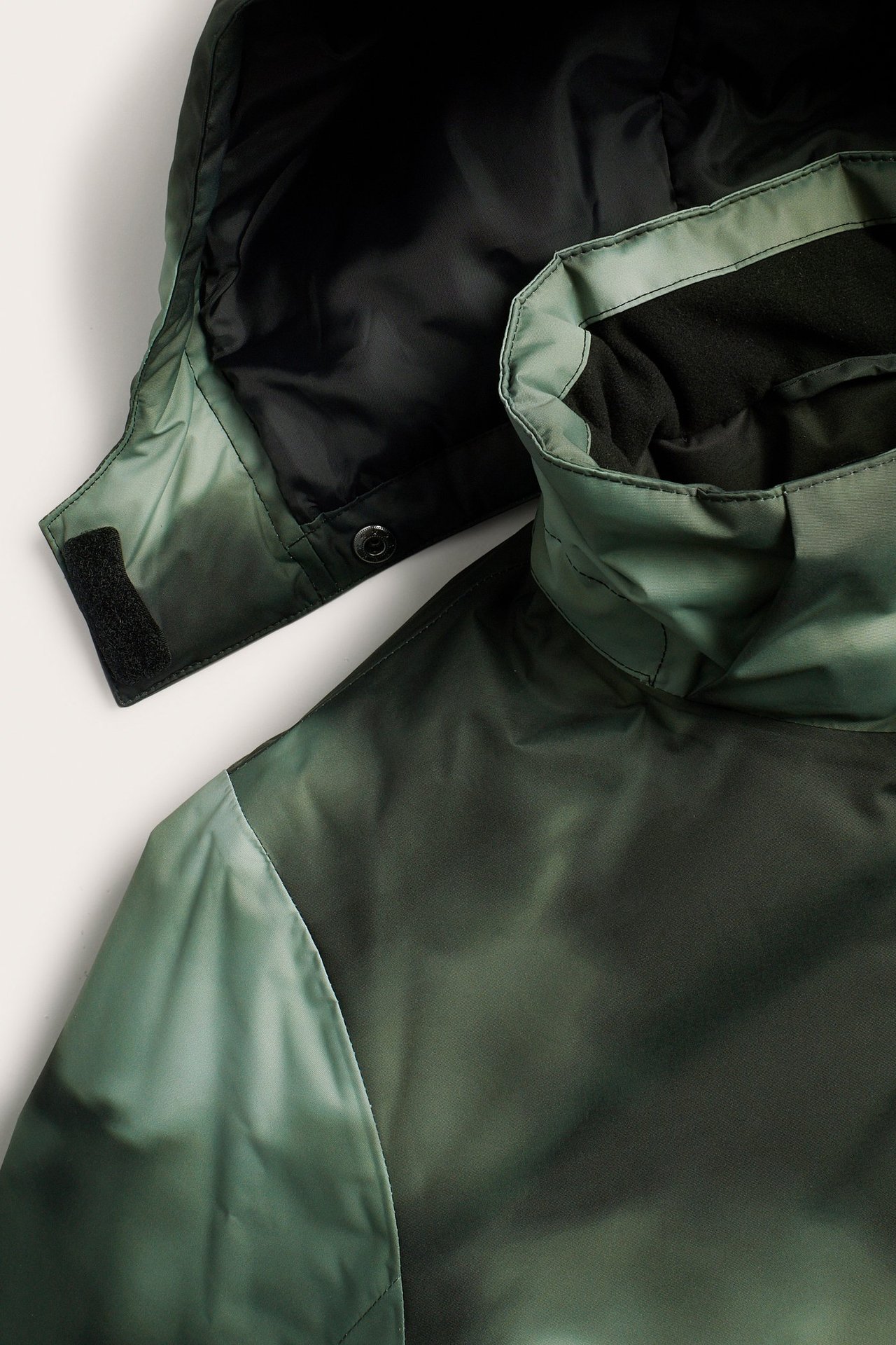 Zbliżenie wzorzystej zielonej kurtki zimowej z wysokim kołnierzem, zapięciem na zatrzaski kaptura i mankietem na rzep.