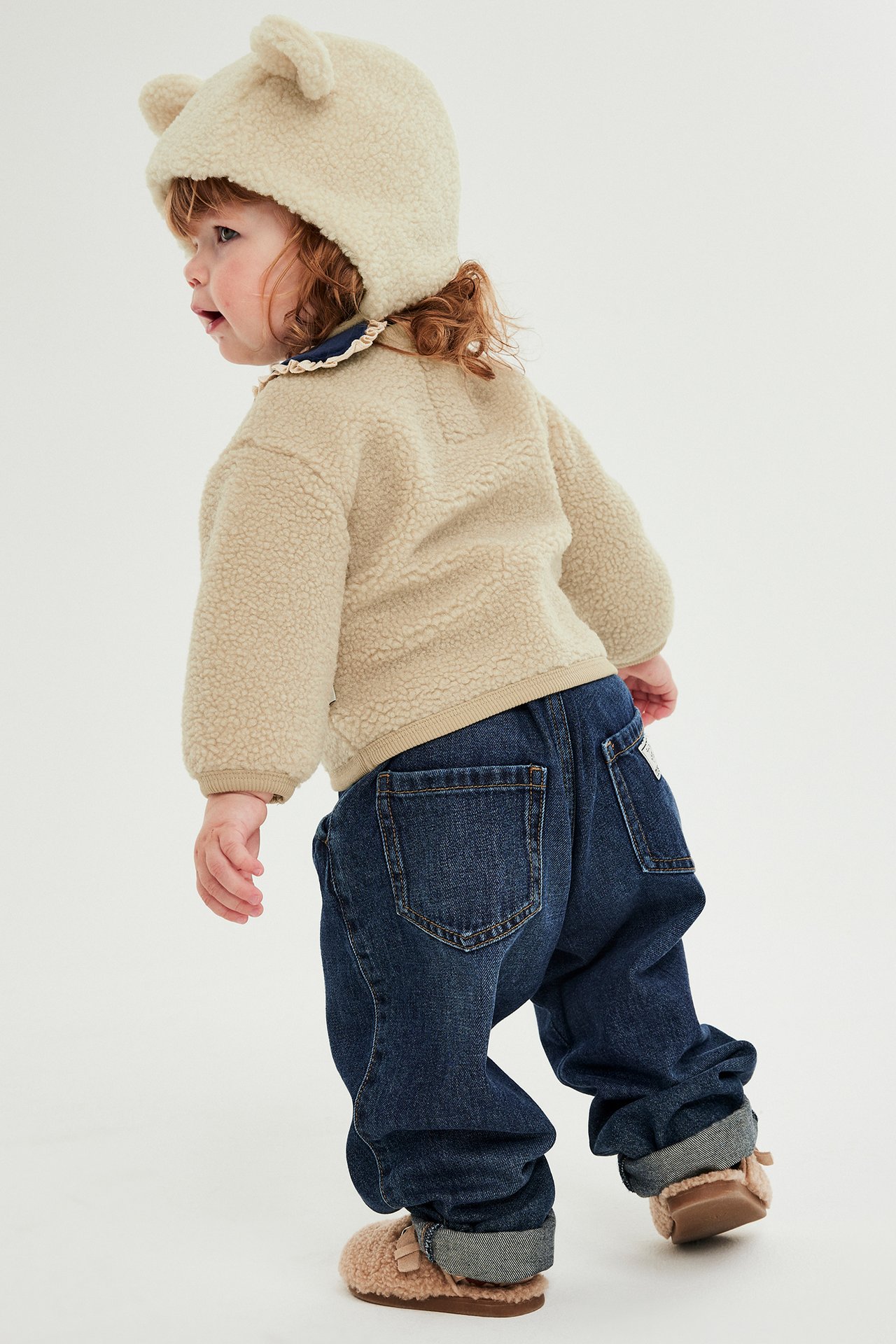 Beige pilekofta med knappar, på liten flicka i jeans och mössa.