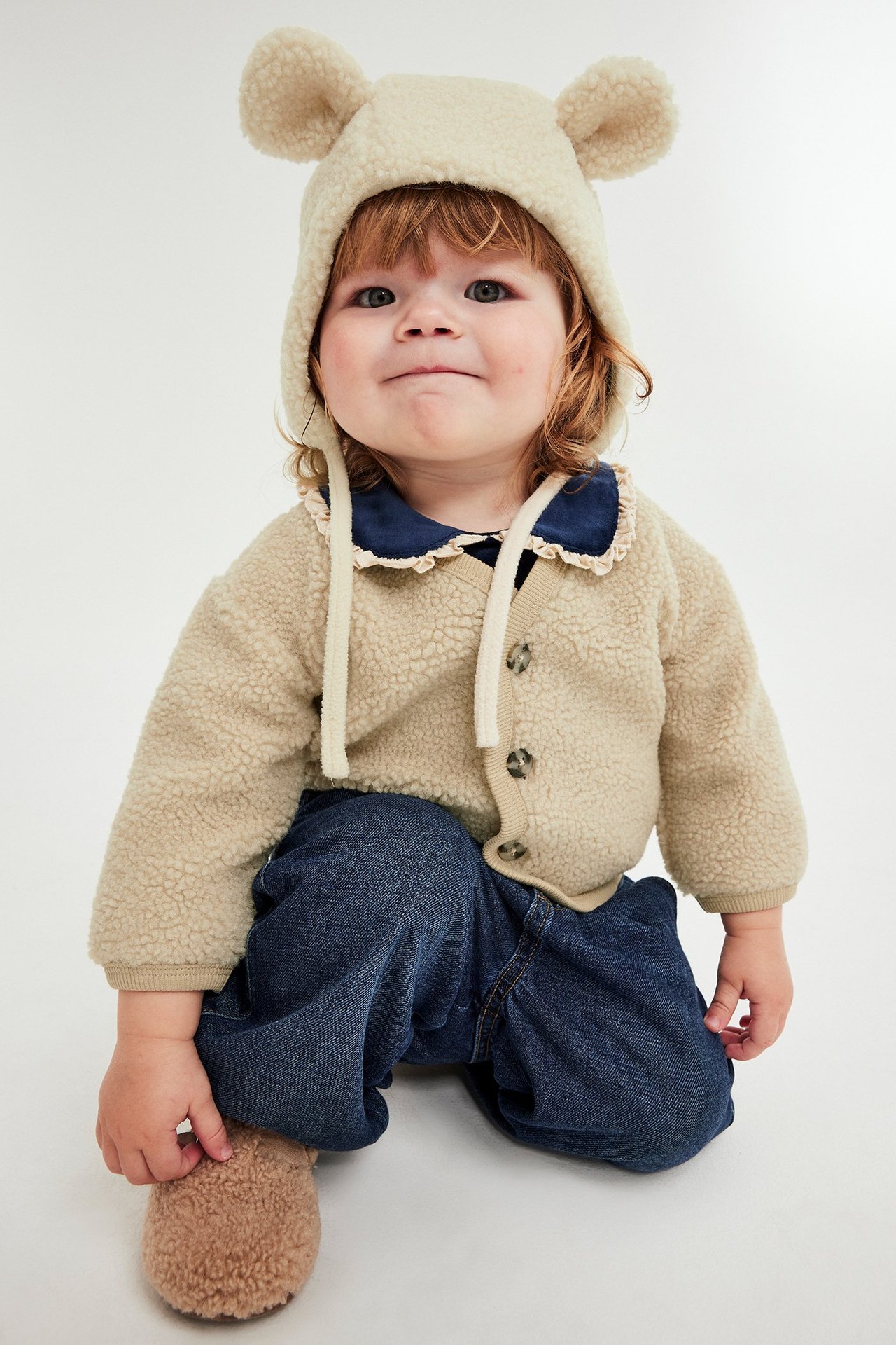 Babykulla i pile med knappar, beige, bärs med blå tröja och mörkblå jeans.