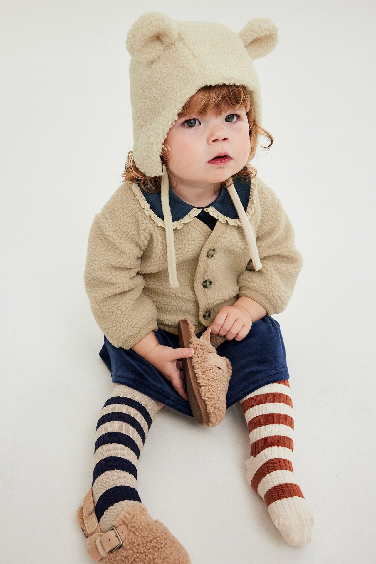 Beige fleece neuletakki paininjemmin, yksivärinen, vauva, etunäkymä, päällä sininen paita.