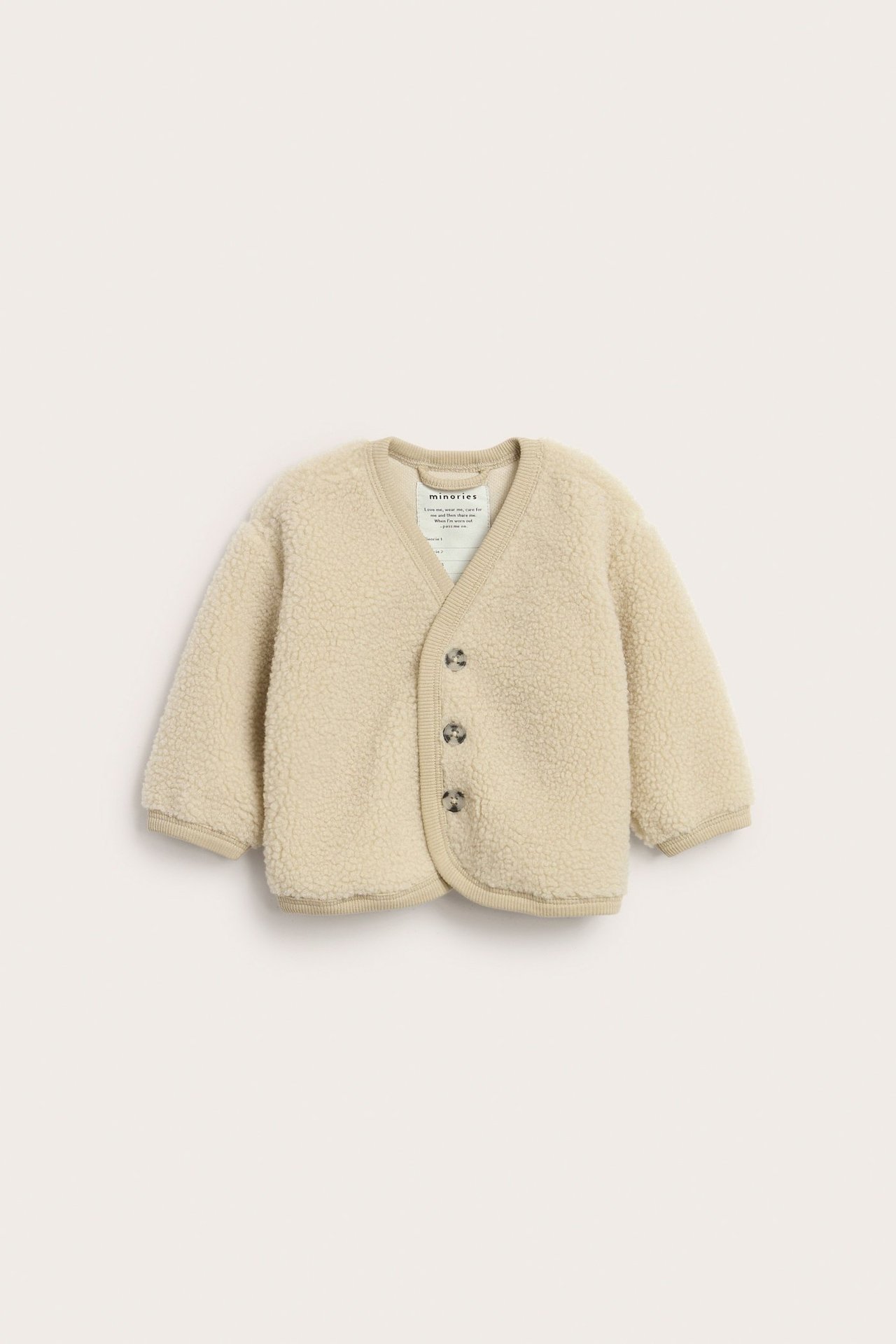 Beige pilekofta med knappar på vit bakgrund, enfärgad, baby, framifrån.