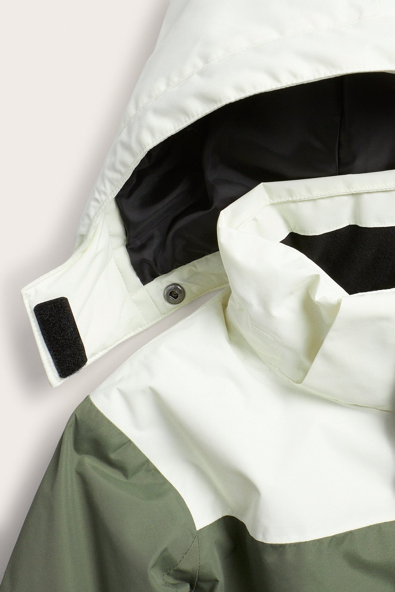 Zbliżenie na zimową kurtkę w bloki kolorów ecru i oliwkowej zieleni, z odpinanym kapturem i czarną podszewką.