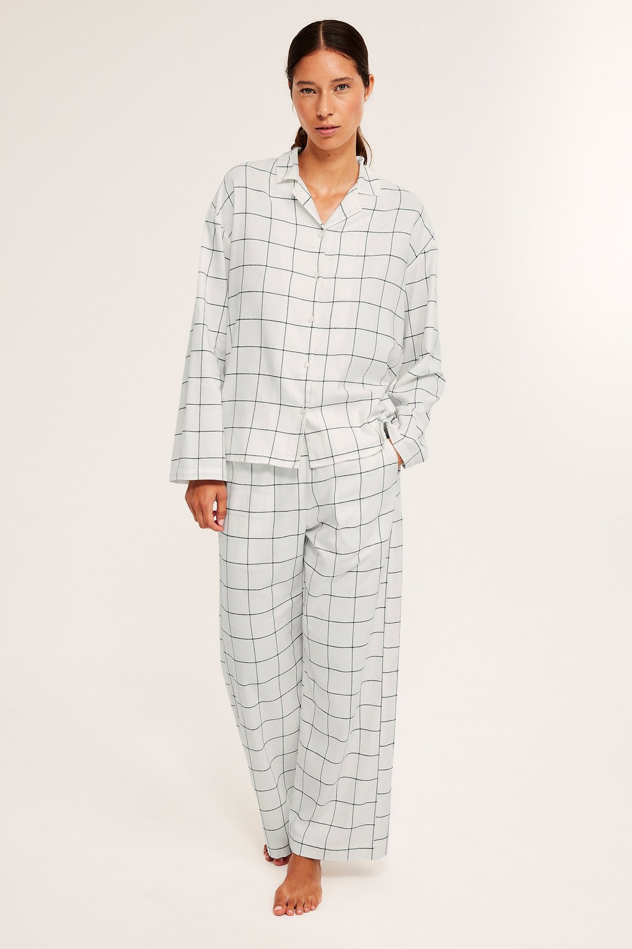 Nainen valkoisissa ruutuhaalari-pyjamasissa, rento istuvuus, etunäkymä.