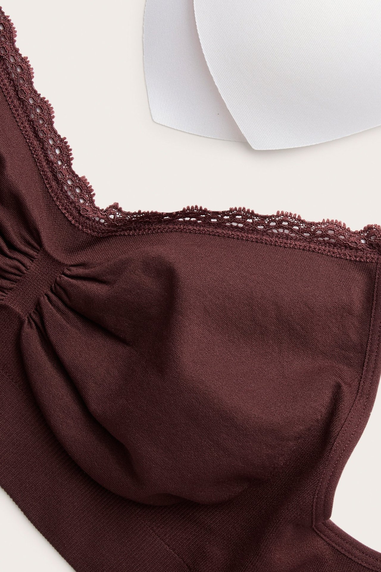 Zbliżenie na bordowy, bezszwowy biustonosz bez fiszbin z koronkową lamówką i dwiema białymi, wyjmowanymi wkładkami.