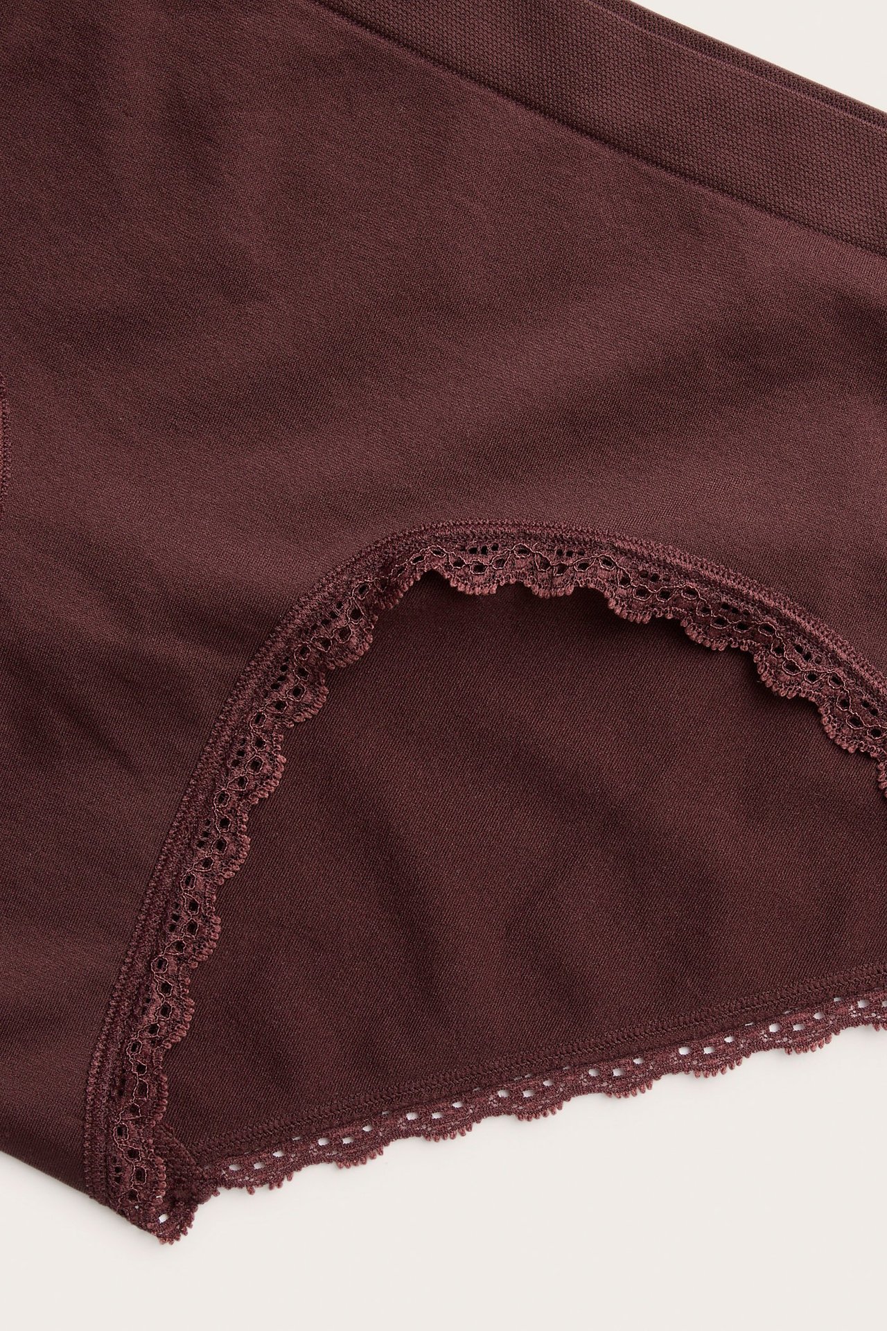 Zbliżenie na bordowe, bezszwowe figi typu hipster z delikatną koronkową lamówką.
