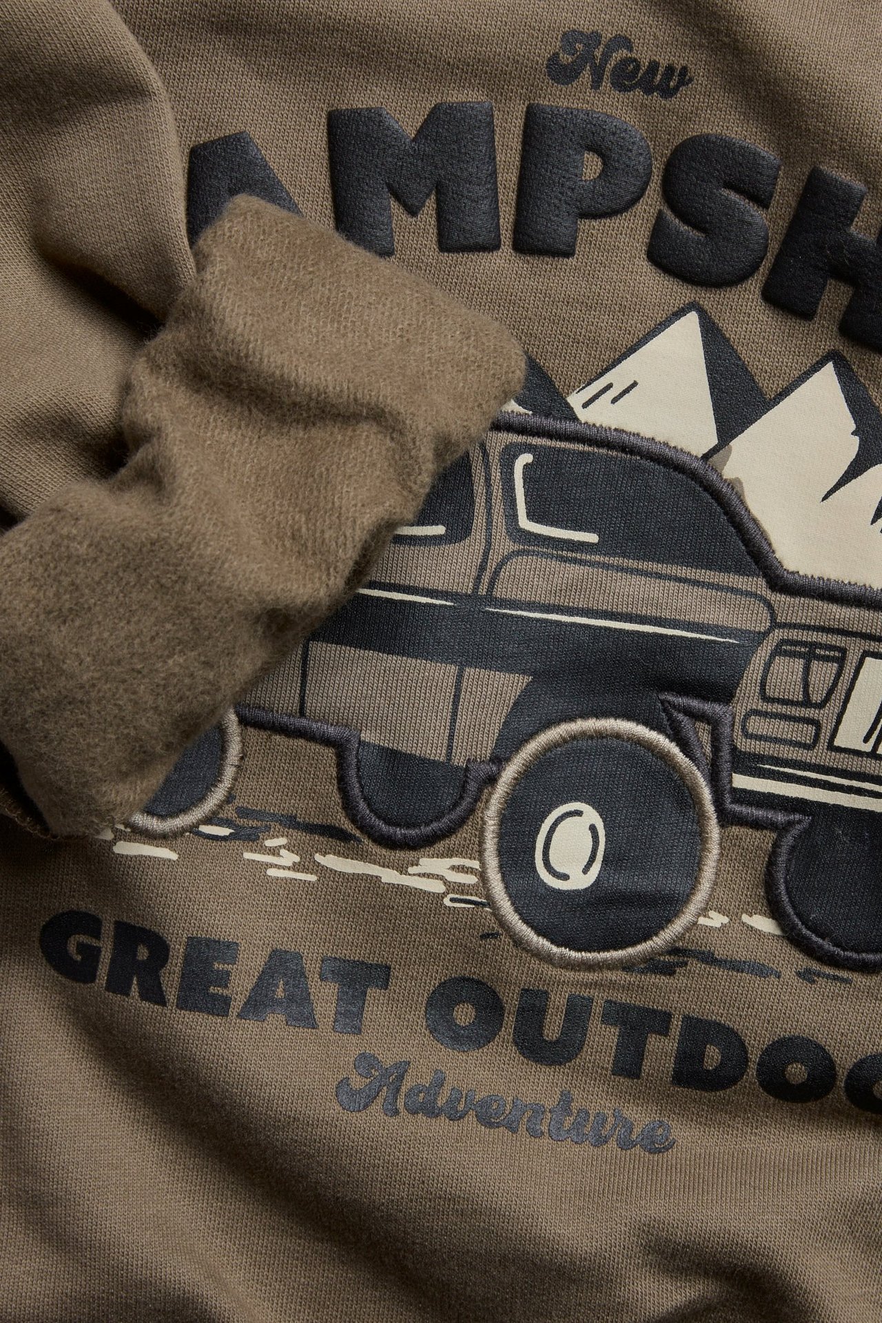 Nærbilde av en brun bomullssweatshirt for barn med myk børstet innside og kjøretøyapplikasjon.