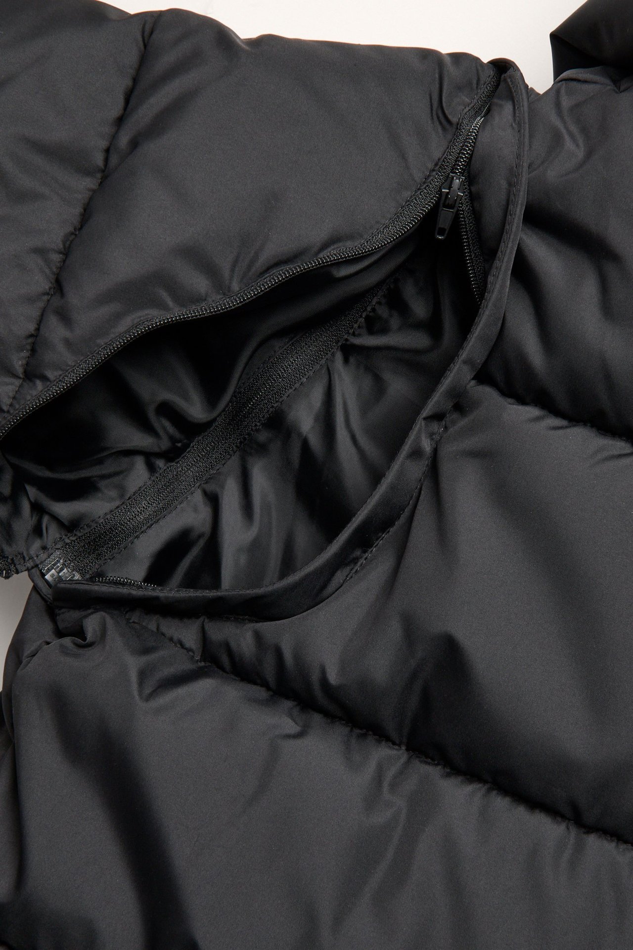 Zbliżenie czarnej kurtki puchowej, ukazujące zamek błyskawiczny na odpinaną część.