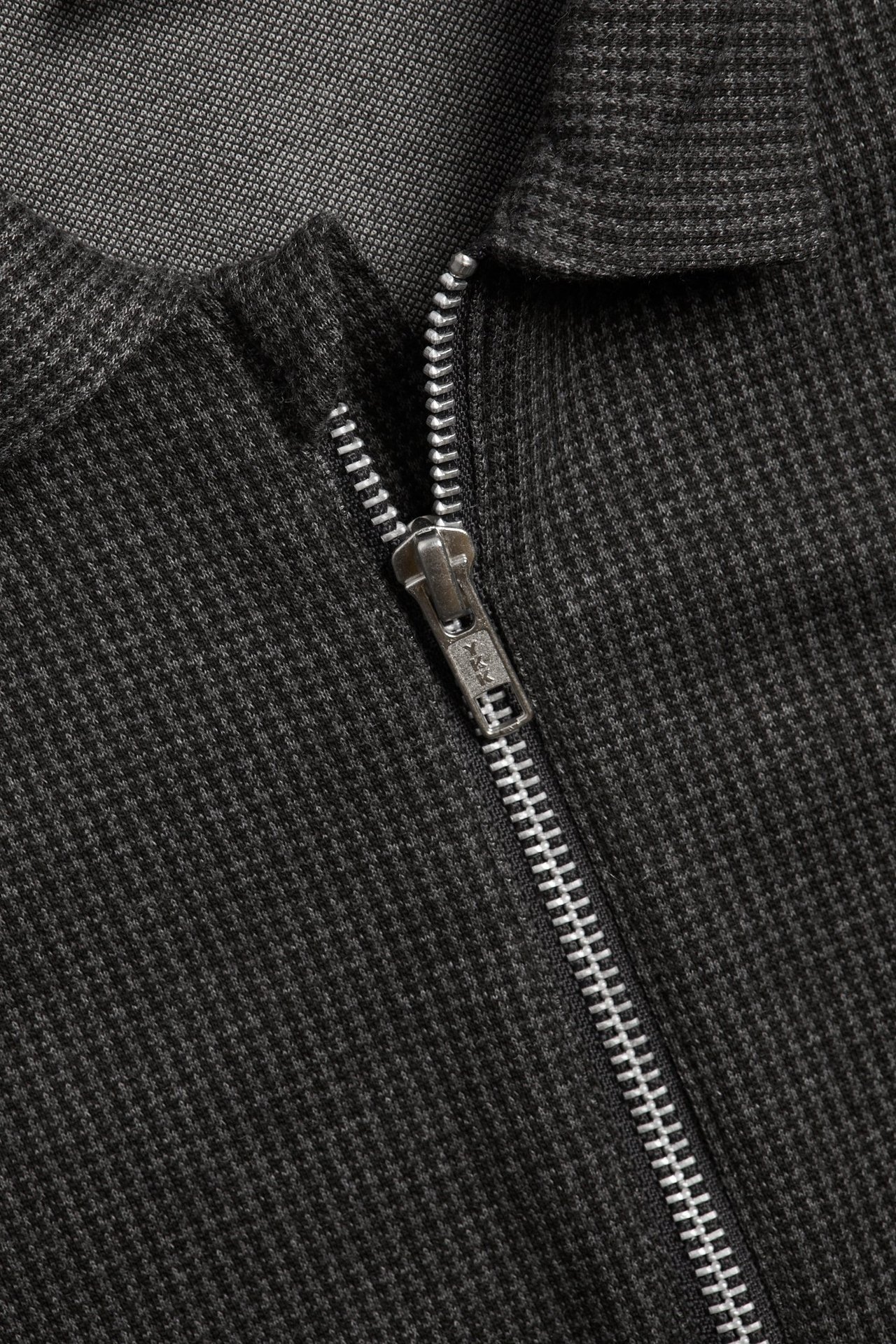 Zbliżenie ciemnoszarej koszuli w kratę houndstooth z metalowym srebrnym zamkiem błyskawicznym.