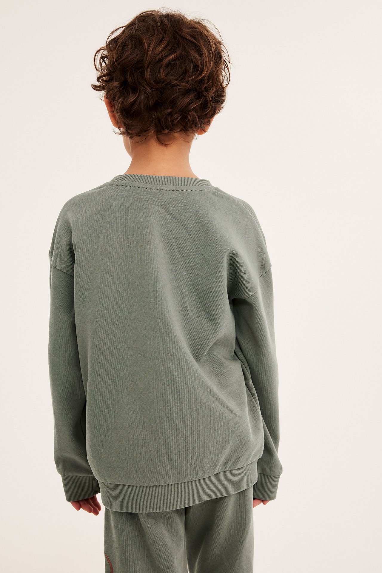 Bakifrån på ett barn i en grön bomullssweatshirt och matchande gröna sweatpants.