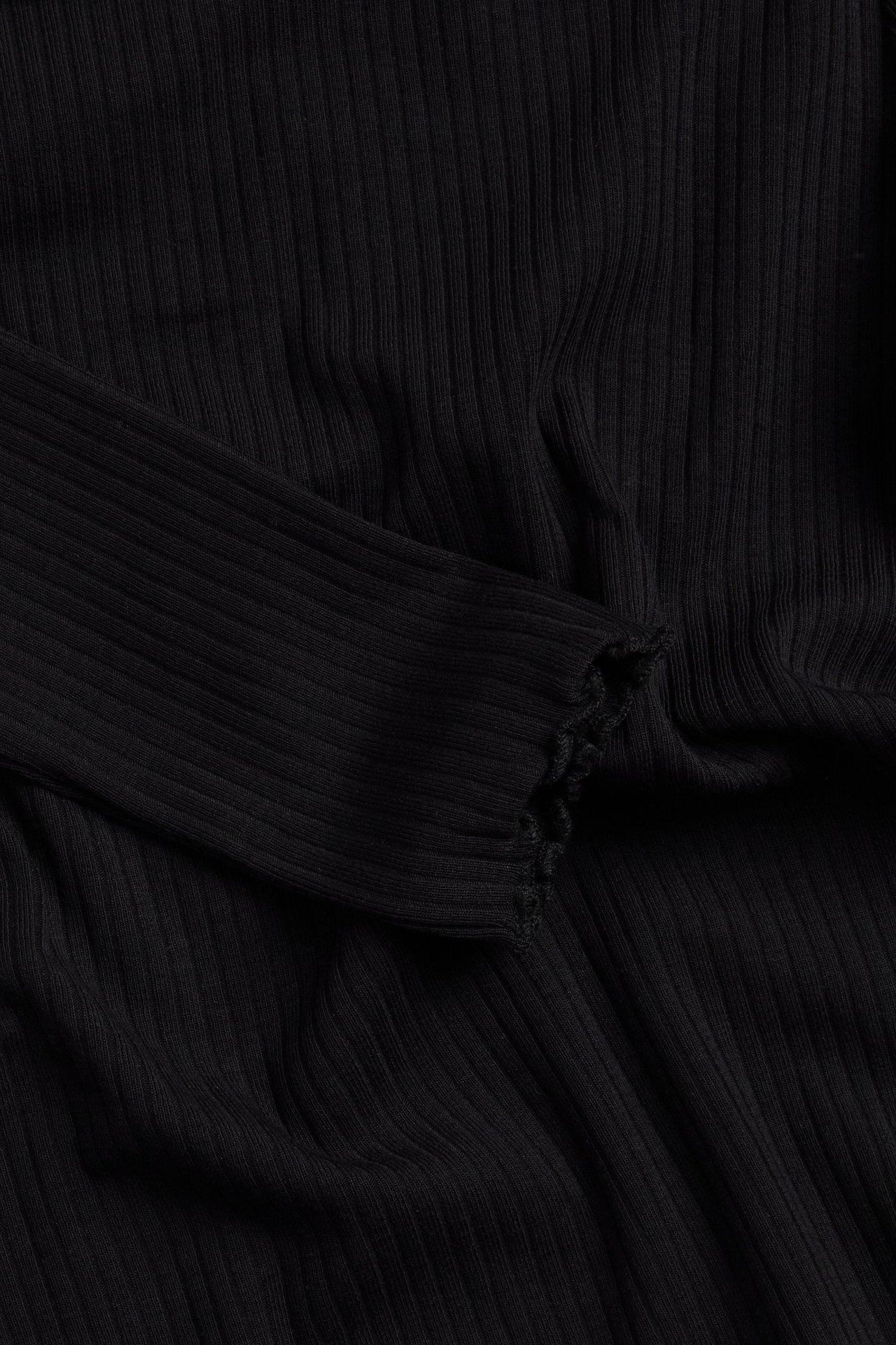 Zbliżenie czarnego, prążkowanego topu z długim rękawem i falbanowym mankietem.