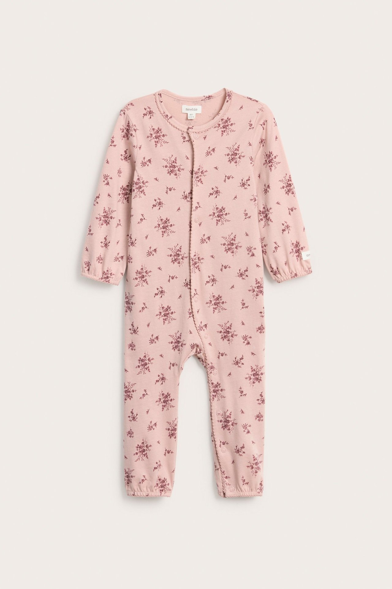 Edestä: vaaleanpunainen puuvillainen vauvan pyjama, jossa sävy-sävyyn kukkakuvio ja nepparit edessä.