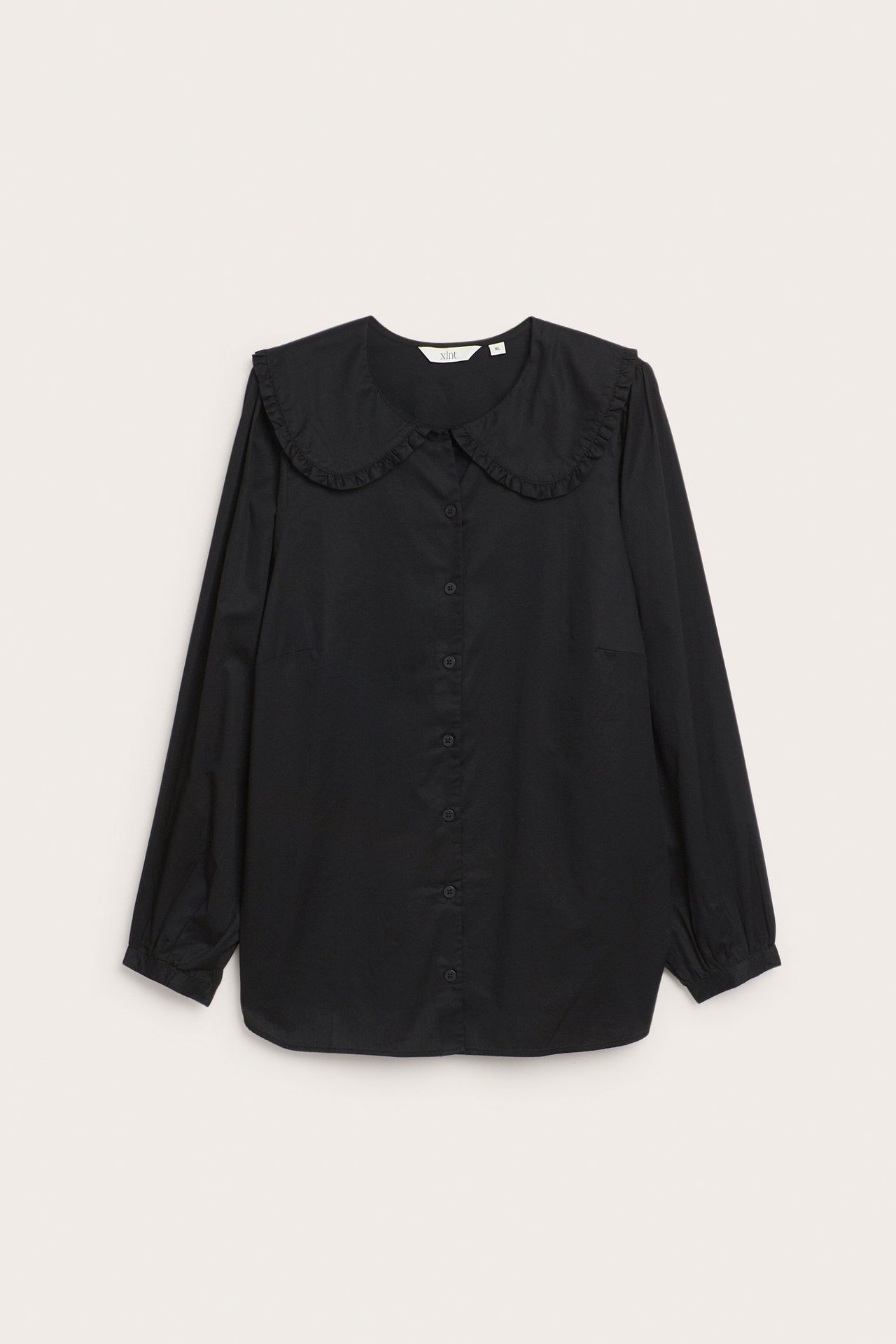 Framifrån, svart bomullsblus med stor rundad, volangkantad krage och knäppning fram.