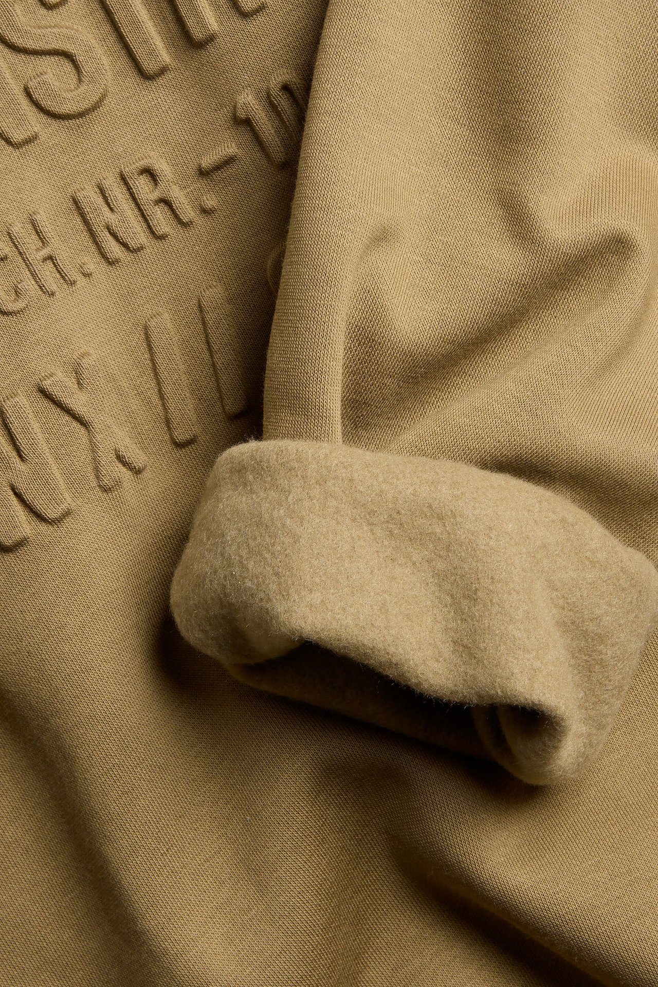 Zbliżenie brązowej bluzy z bawełny z efektem 3D i widocznym szczotkowanym wnętrzem mankietu.