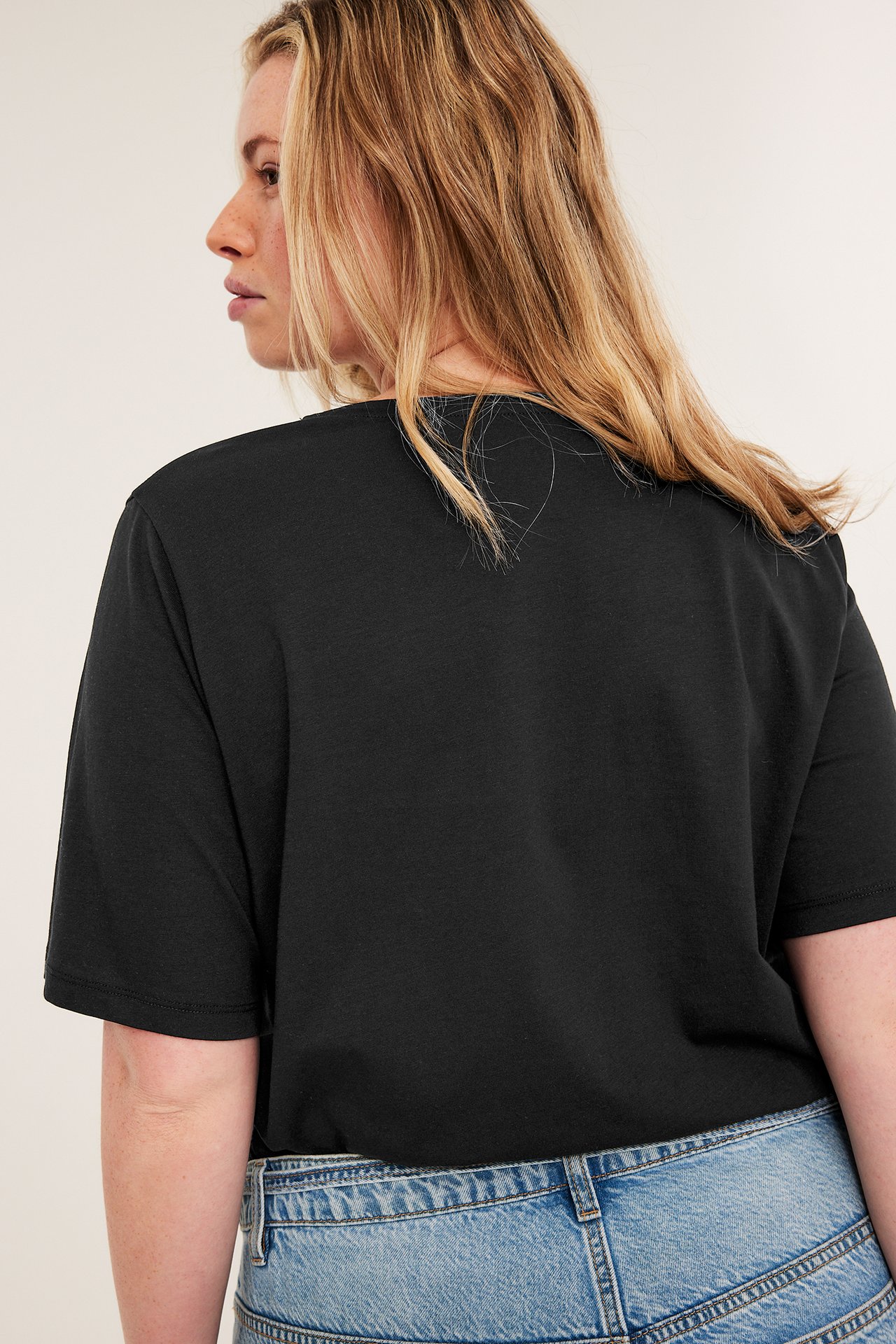 Kobieta tyłem w czarnym, dopasowanym bawełnianym t-shircie i jasnoniebieskich jeansach.