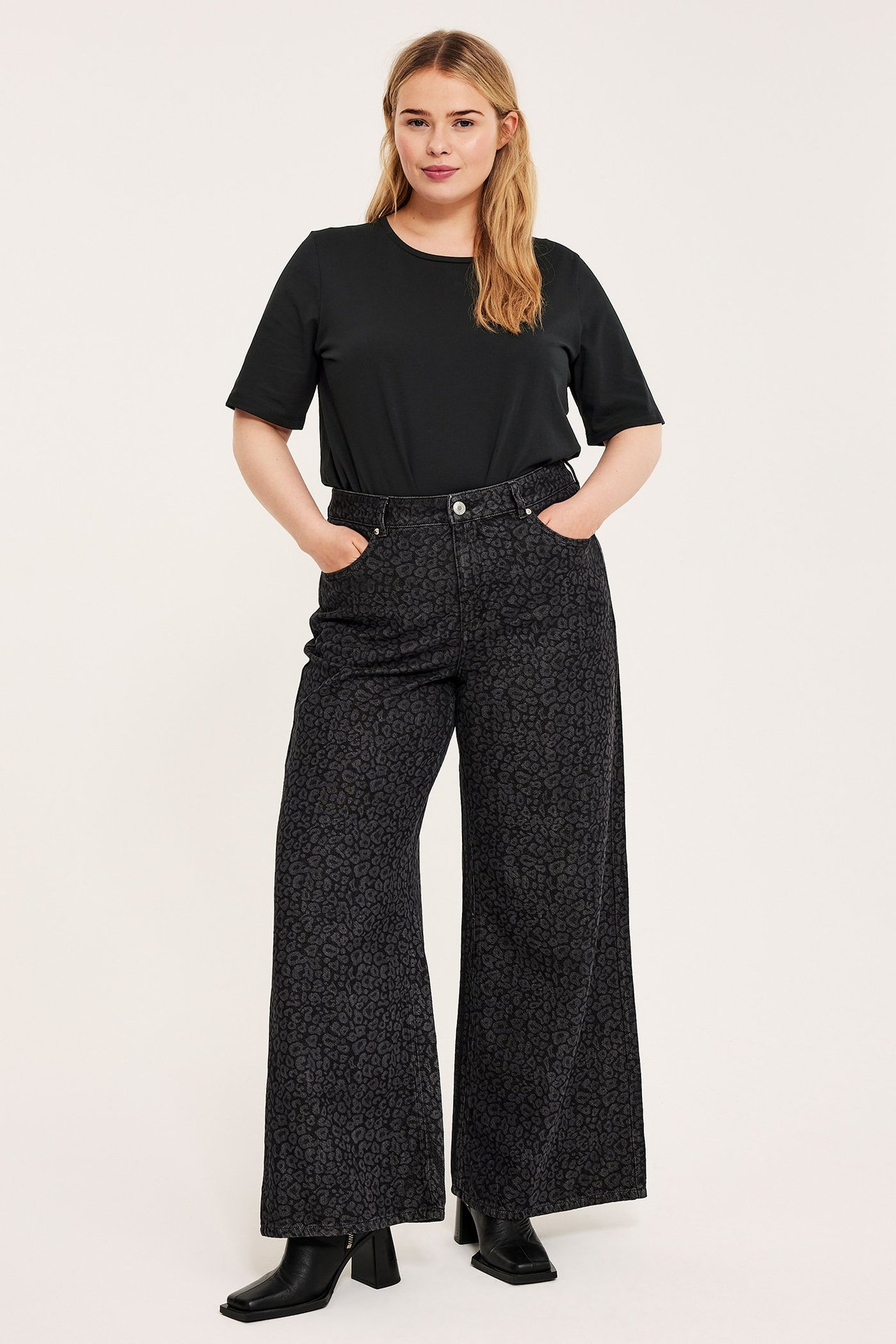 Kvinne i svart T-skjorte, mørkegrå leopardmønstrede vide bukser og svarte ankelstøvler.