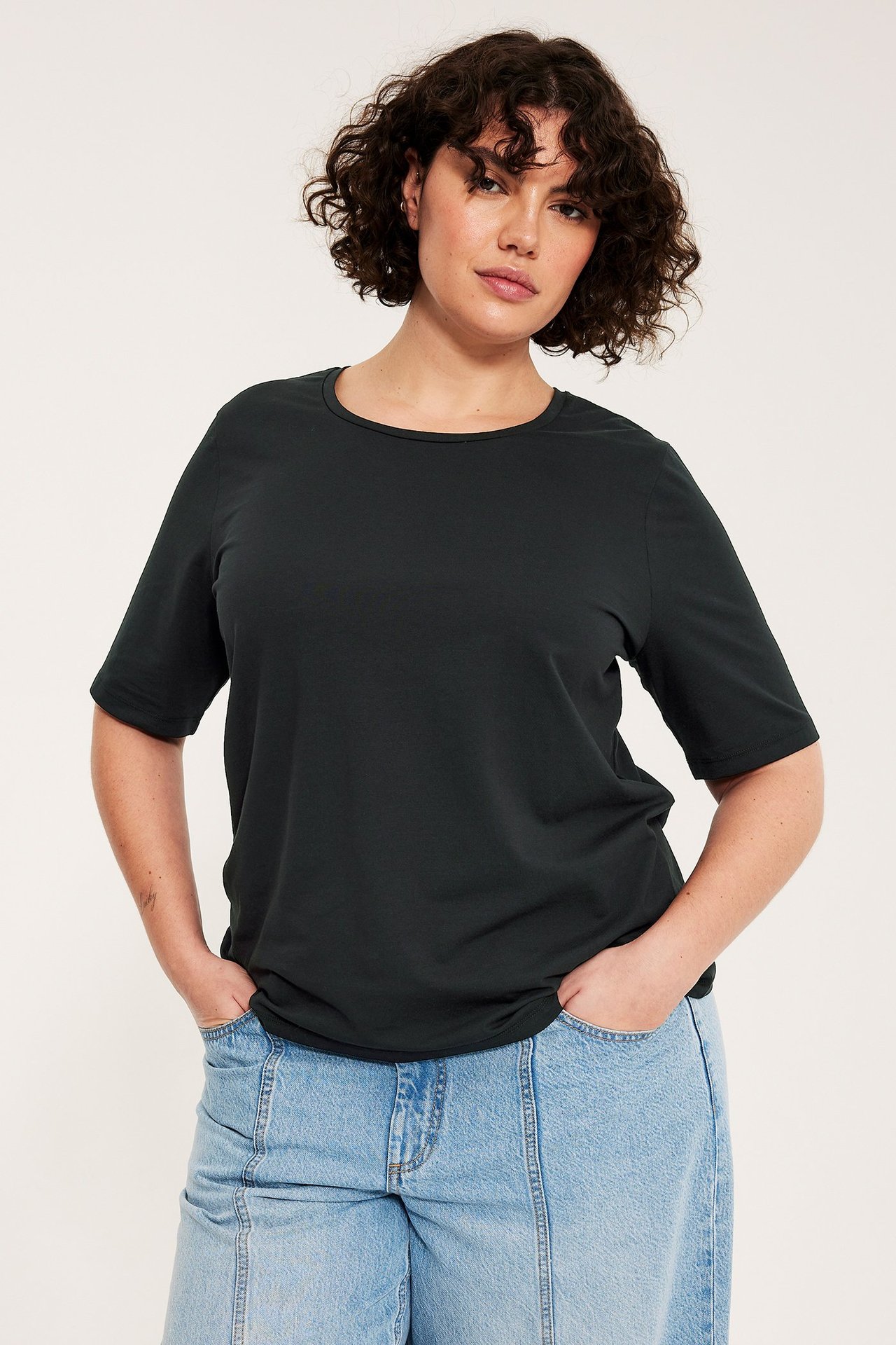 Naisen etunäkymä mustassa, väljässä T-paidassa, jossa on pyöreä pääntie, ja vaaleansinisissä farkuissa.