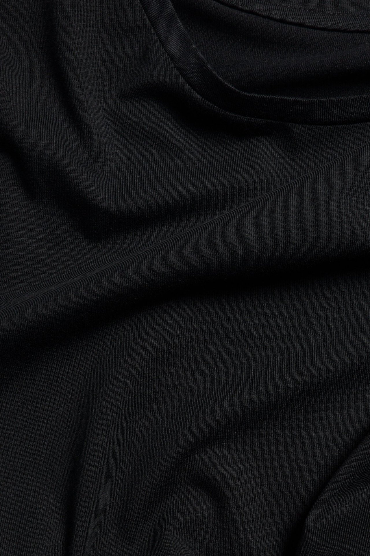 Zbliżenie na czarny, jednolity T-shirt z okrągłym dekoltem, ukazujące fałdy materiału.