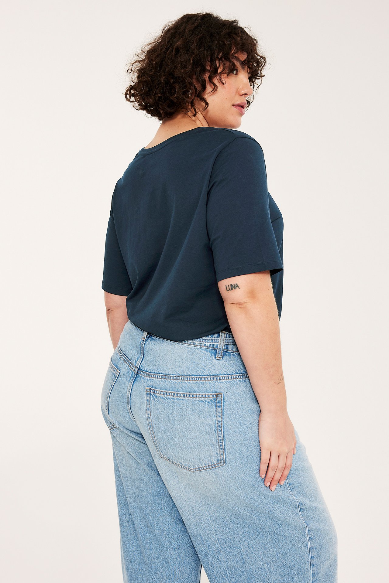 Baksidevisning av en kvinne i en mørkeblå bomulls-T-skjorte og lyseblå jeans.