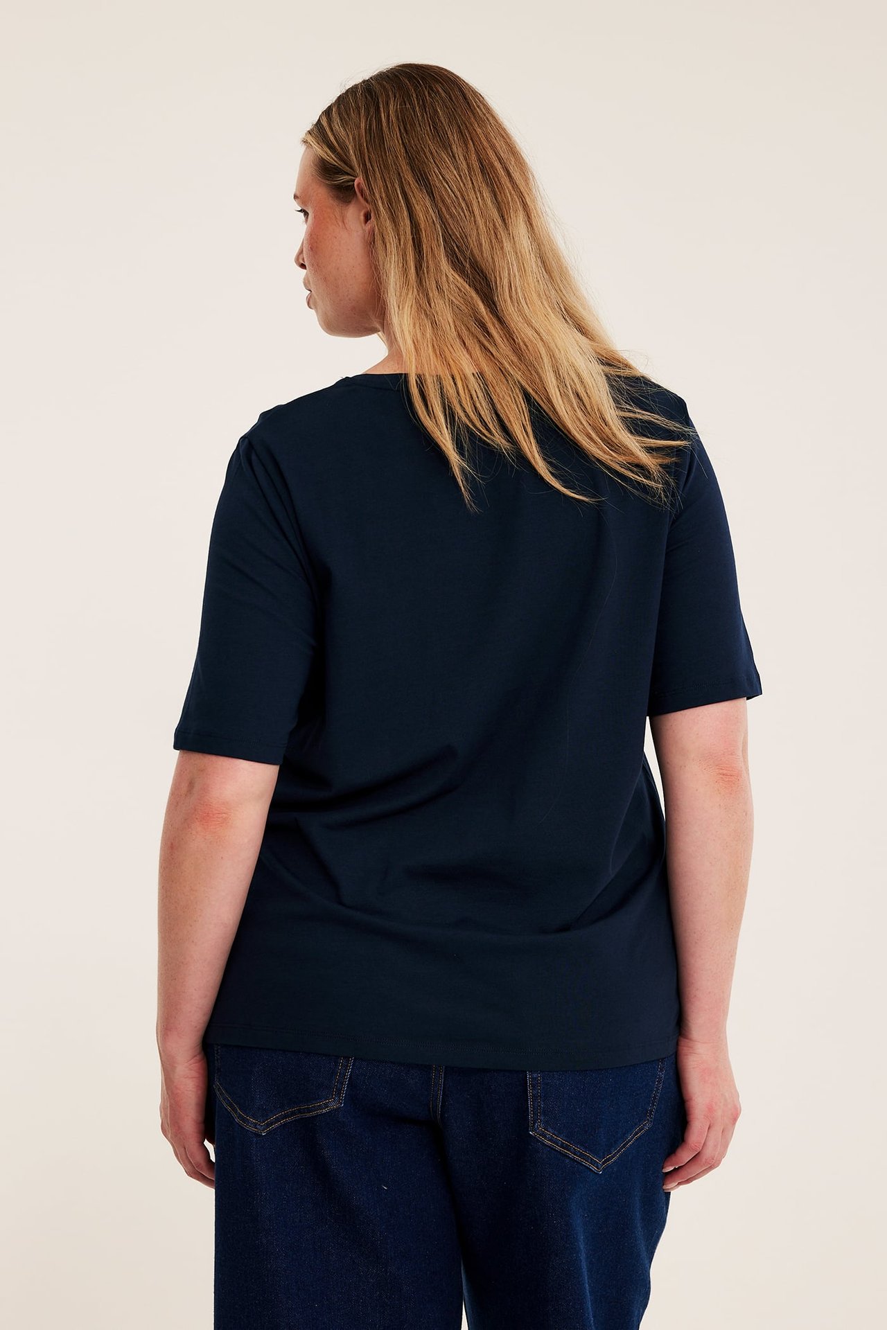 Kvinne bakfra i mørkeblå kortermet t-skjorte og mørkeblå jeans.