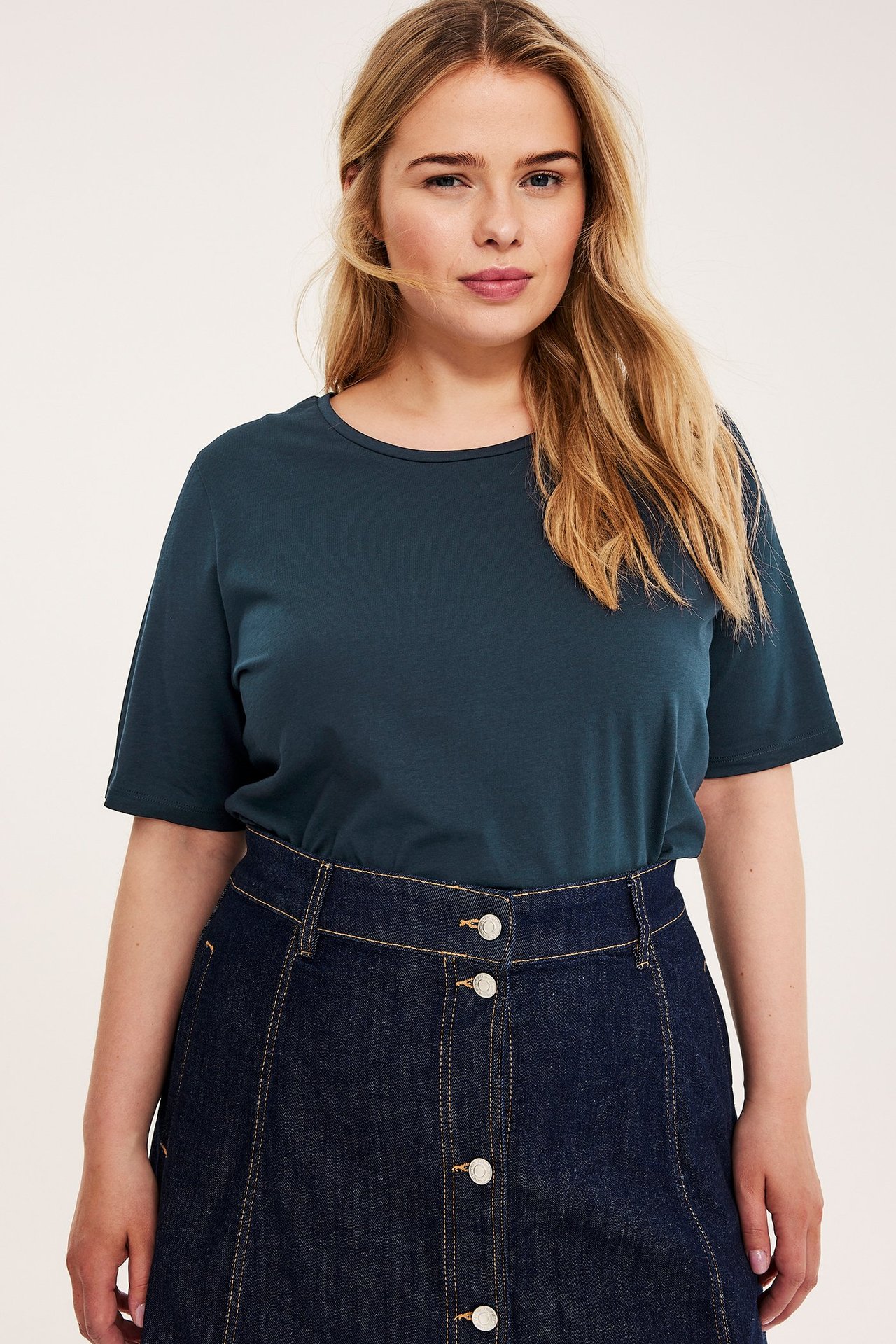 Forfra, en kvinne i en mørkeblå bomulls-T-skjorte og et mørkt denimskjørt med knapper.