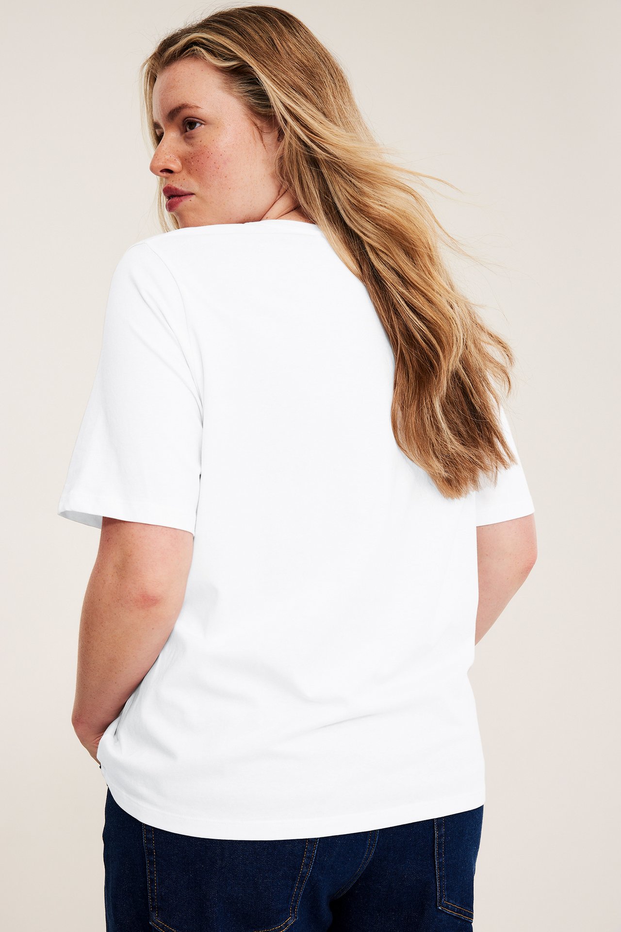 Widok z tyłu kobiety w dopasowanym białym bawełnianym t-shircie i granatowych dżinsach.