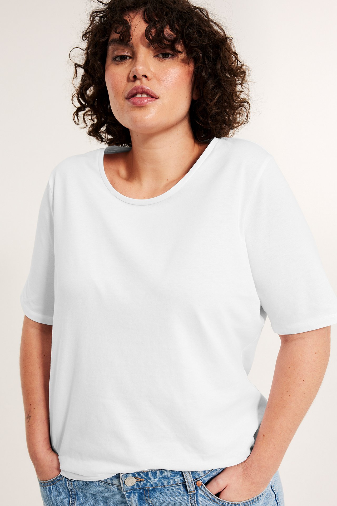 Frontvy av kvinna i vit kortärmad bomulls-T-shirt med rund hals och blå jeans.