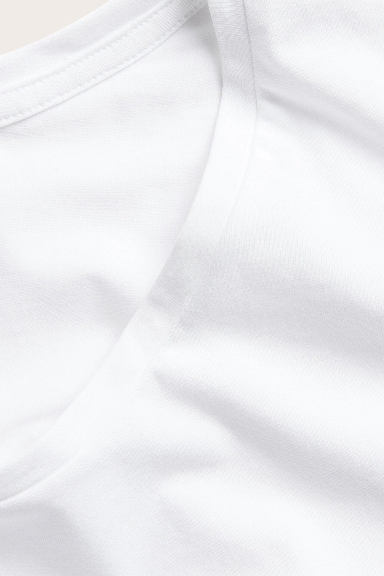 Zbliżenie białego T-shirtu z mieszanki bawełny, ukazujące gładki materiał i prążkowany dekolt.