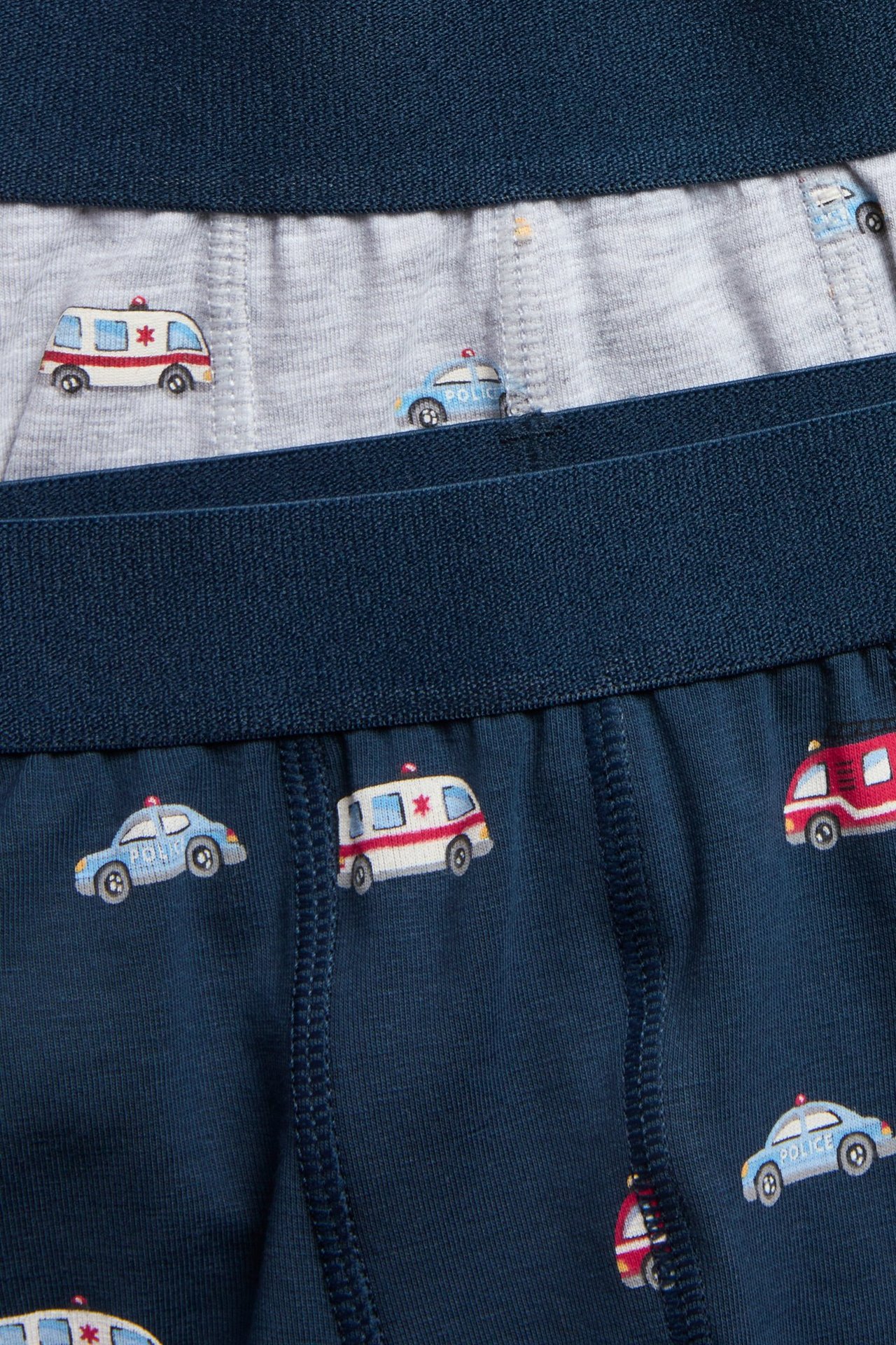 Lähikuva kahdesta parista lasten bokserishortseja: tummansiniset ja vaaleanharmaat, molemmissa ajoneuvokuviot.