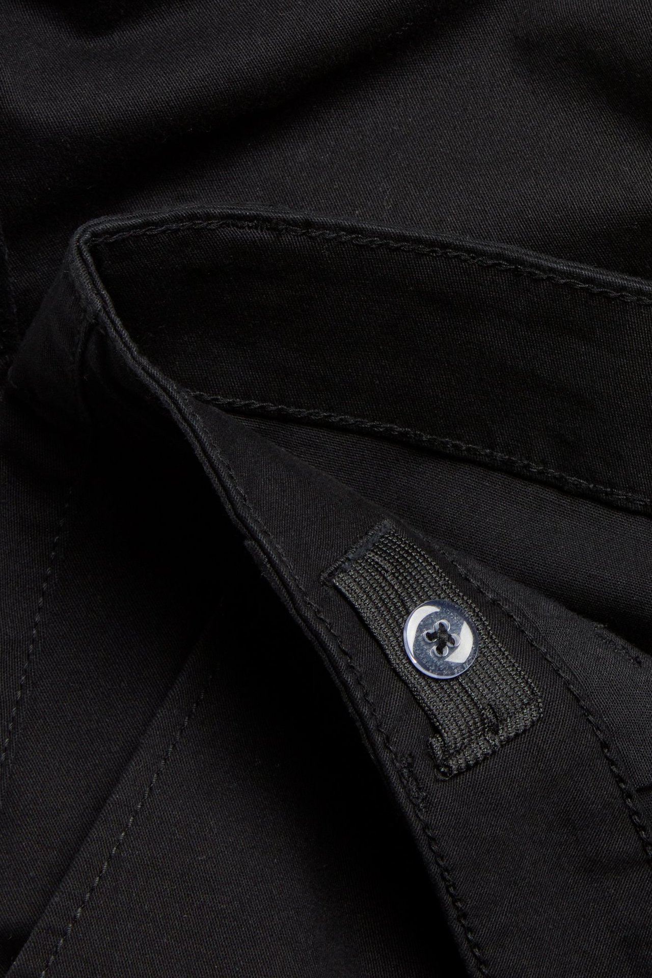 Zbliżenie czarnych bawełnianych spodni cargo z regulowaną gumką i guzikiem w pasie.
