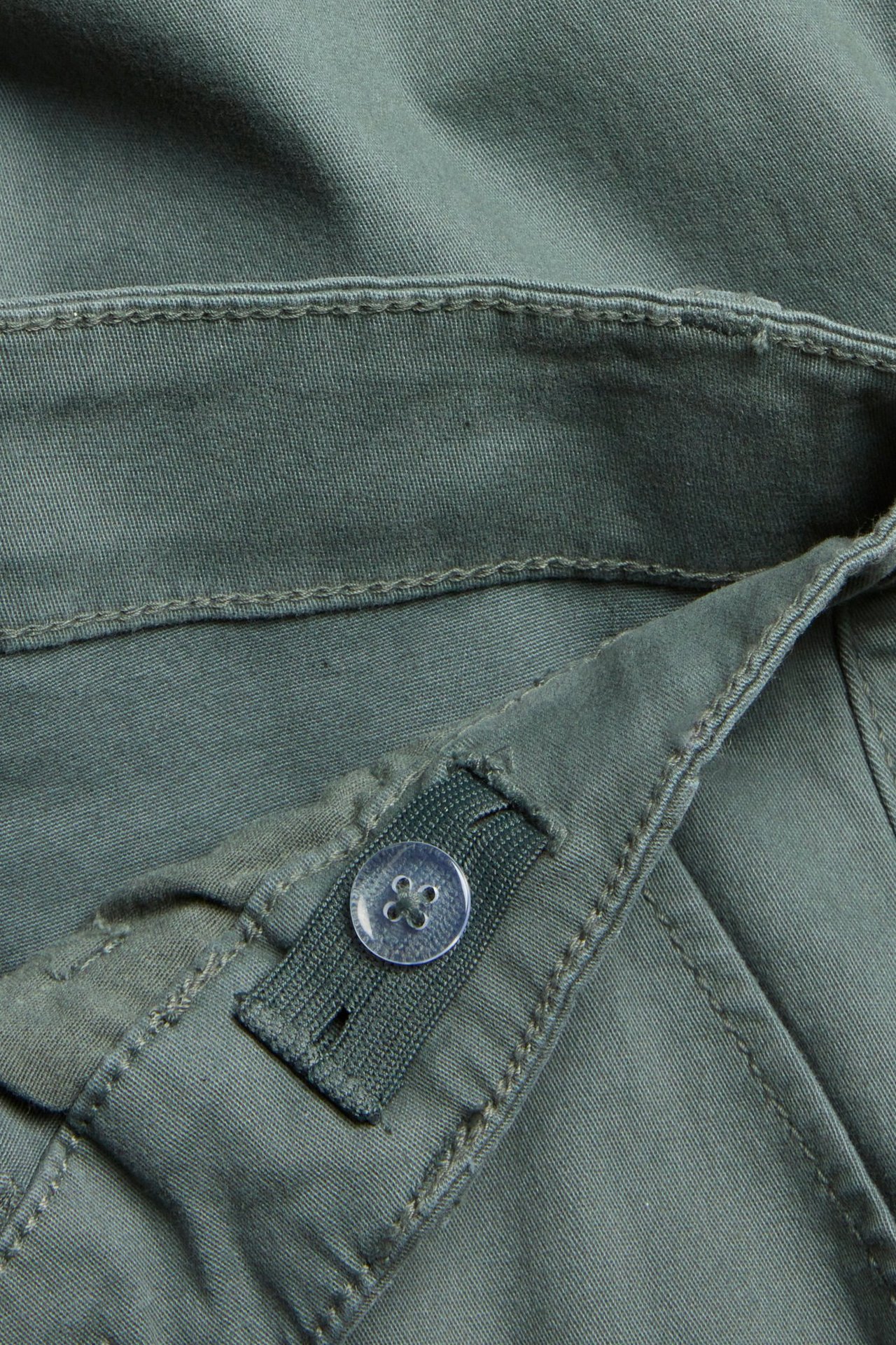 Zbliżenie na zielone bawełniane spodnie cargo, pokazujące przezroczysty guzik na elastycznym pasie.