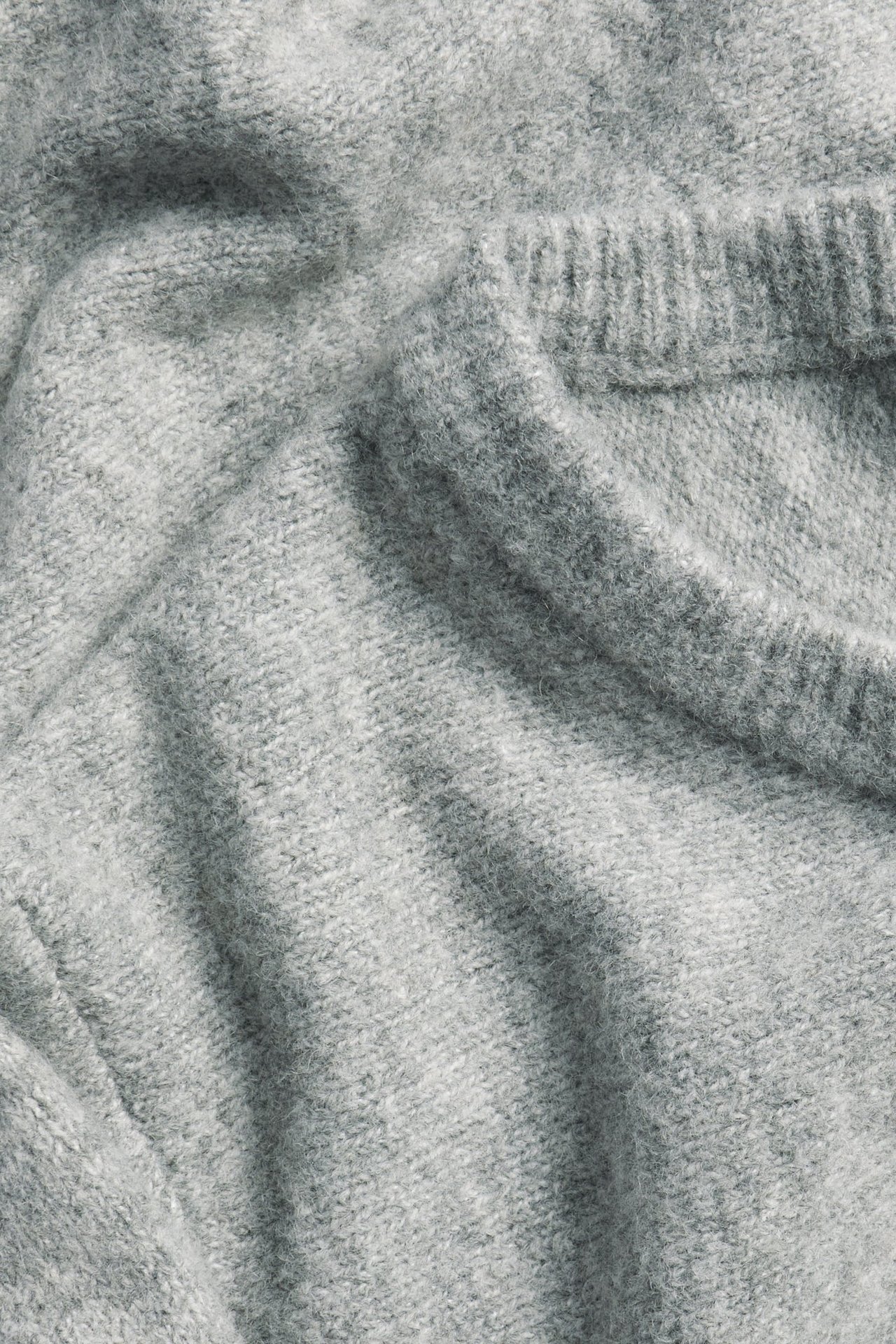 Zbliżenie na jasnoszarą dzianinę sukienki, ukazujące jej miękką, jednolitą teksturę.