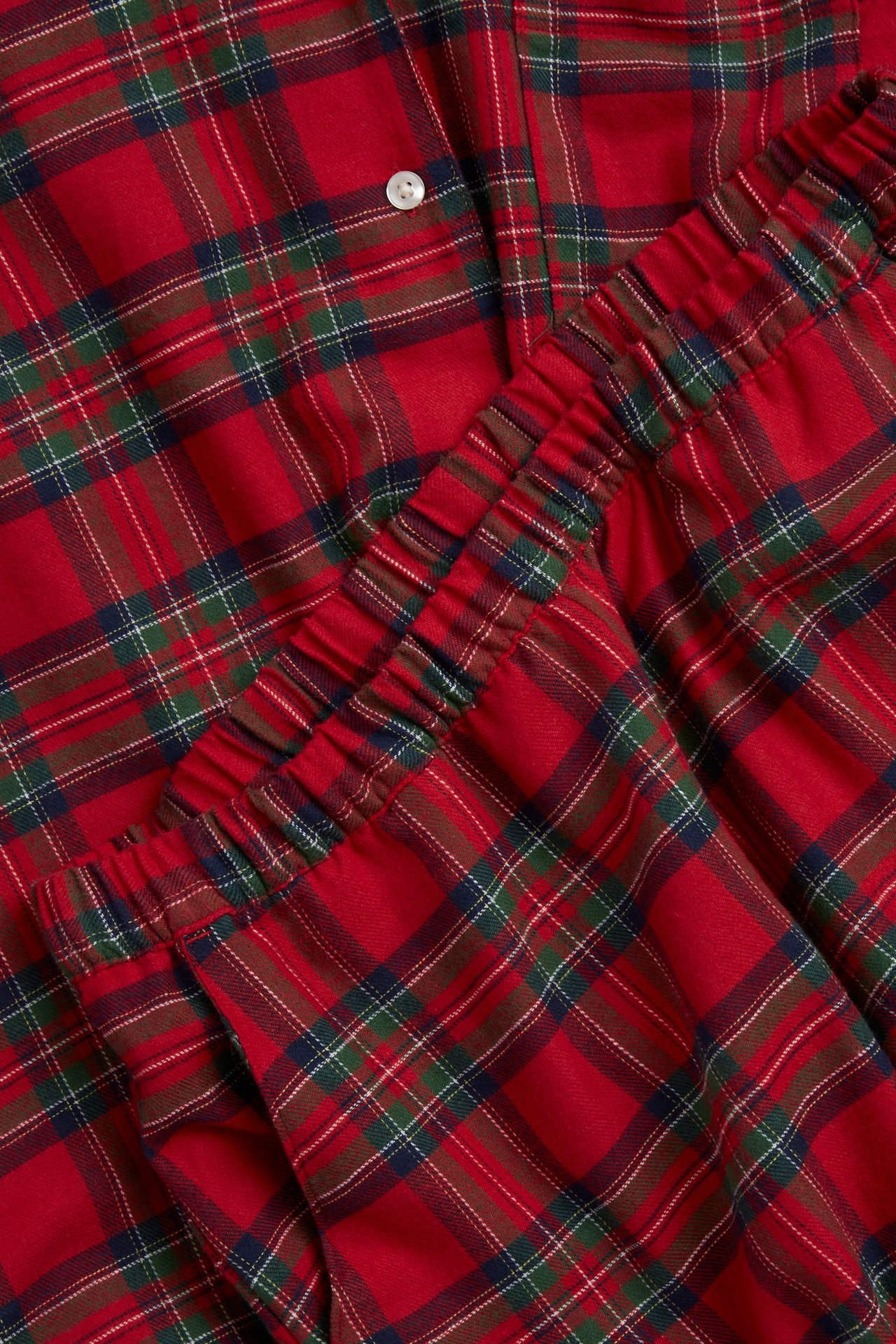 Nærbilde av rød rutete flanellpyjamas med knappet overdel og bukser med elastisk midje.